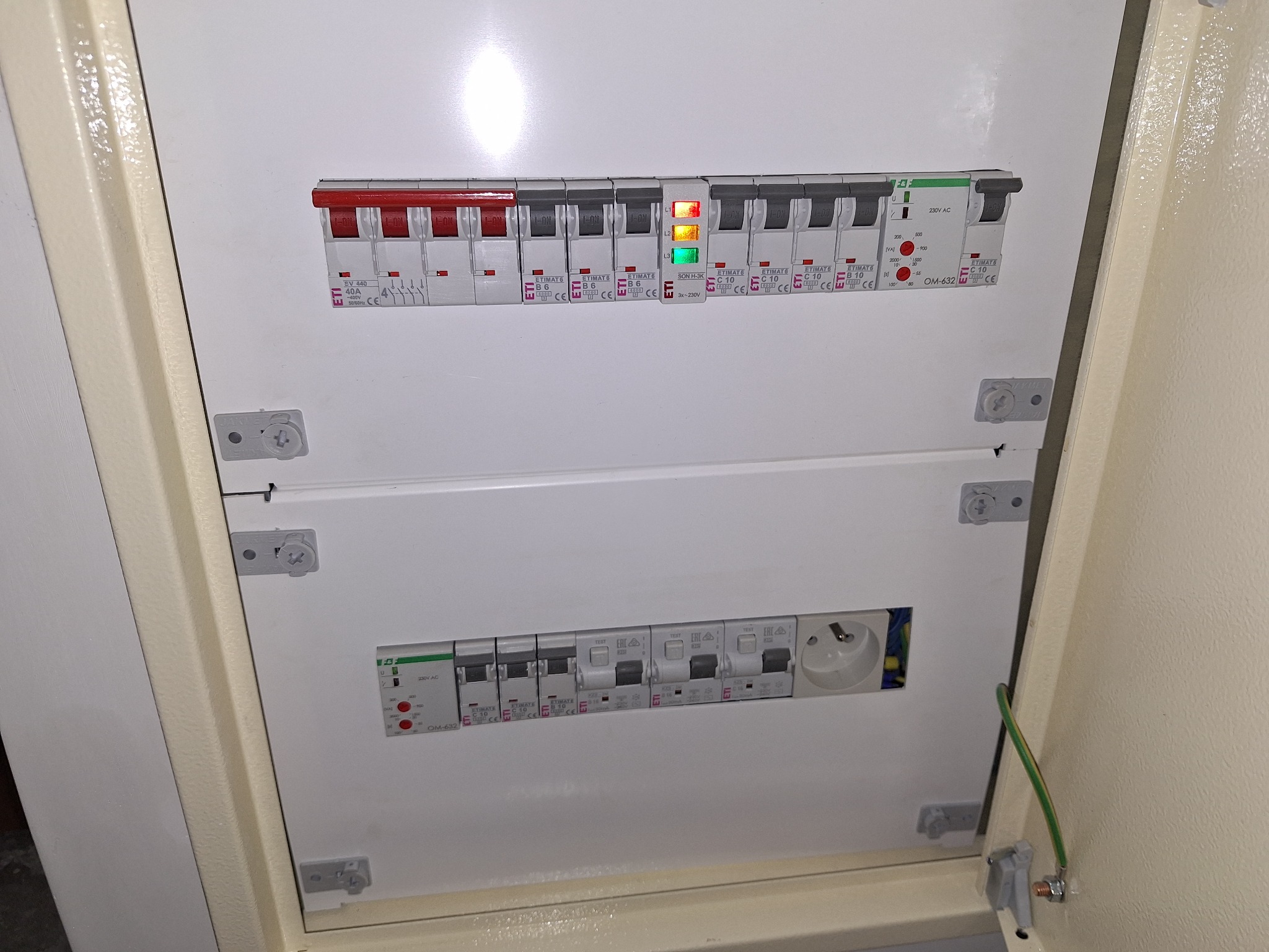 Rozdzielnia elektryczna z bezpiecznikami ETI, widoczne zabezpieczenia różnicowoprądowe i nadprądowe, gniazdo, oraz przewód uziemiający. Instalacja wewnątrz obudowy.