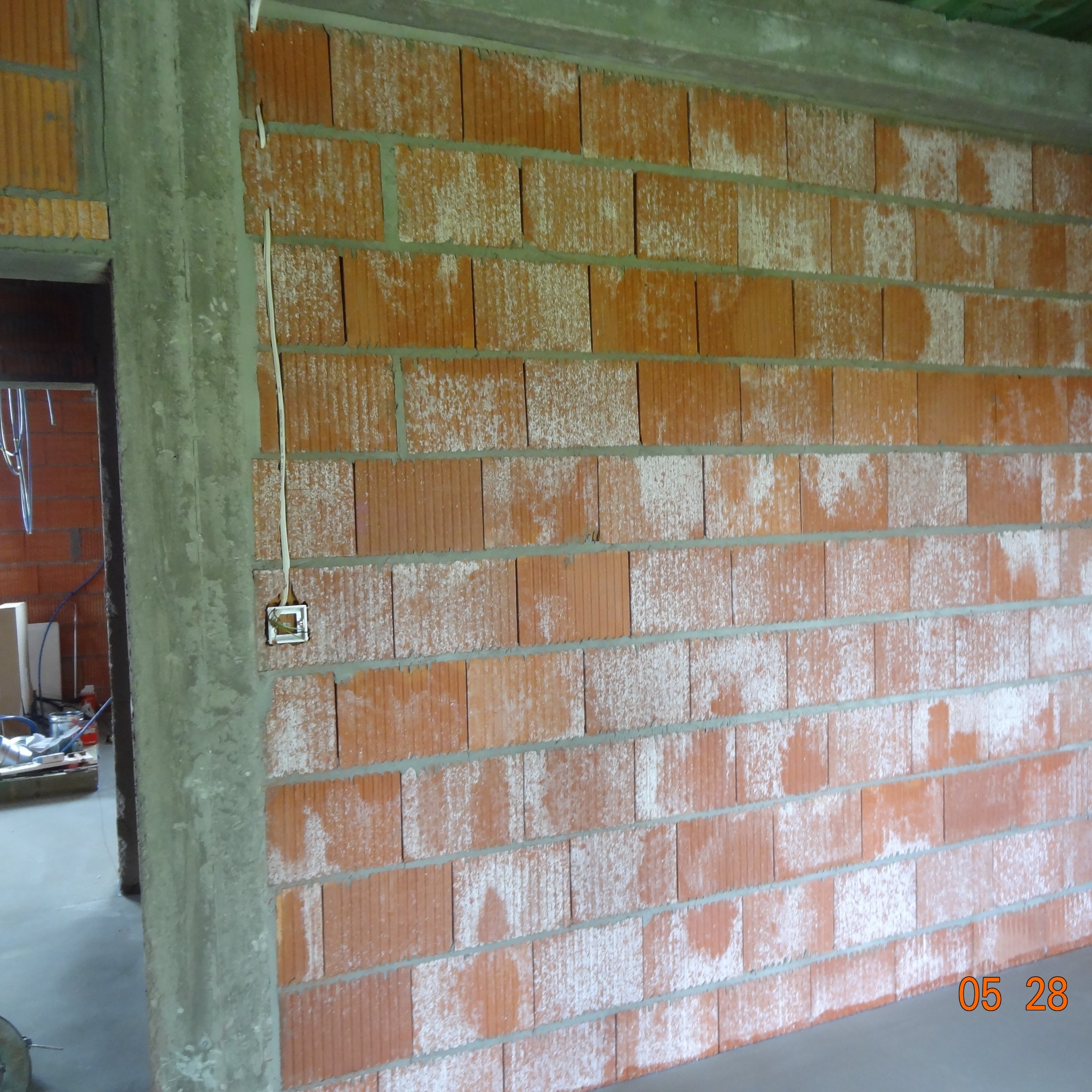 Murowana ściana z pustaków ceramicznych z puszką elektryczną i wystającym kablem, widok z bliska na etapie budowy.