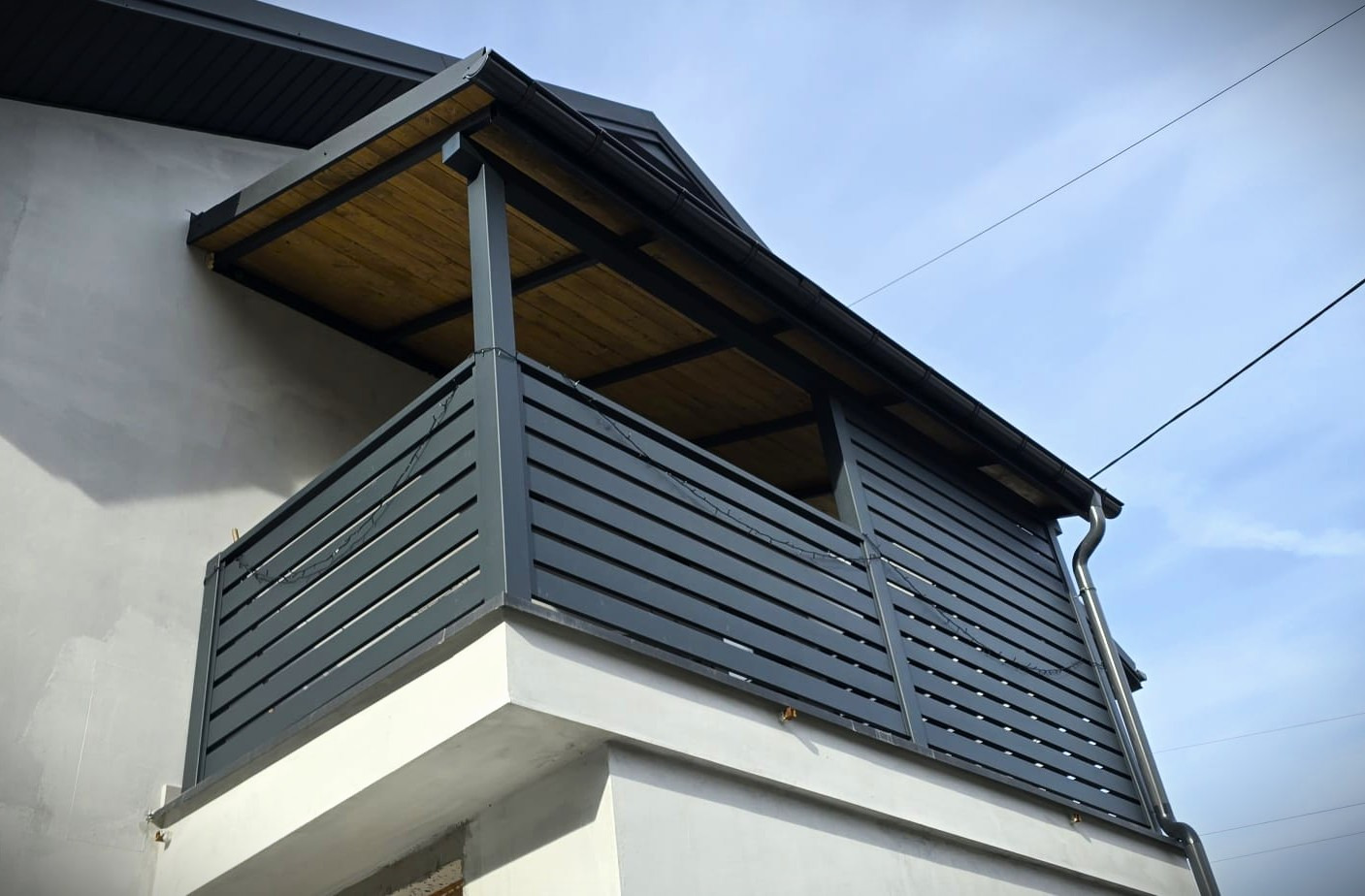 Ciemnoszara, pozioma balustrada zadaszonego balkonu z drewnianym sufitem, widok z dołu, słoneczny dzień, nowoczesny design.