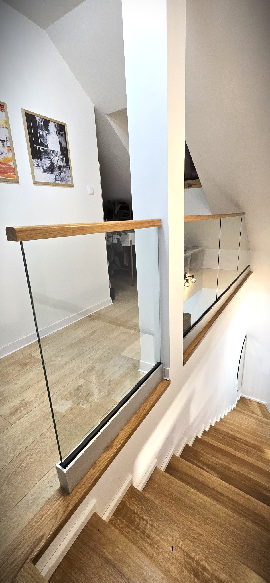 Szklana balustrada z drewnianym wykończeniem na schodach w nowoczesnym wnętrzu. Widok z góry na drewniane stopnie i eleganckie, minimalistyczne wykończenie.