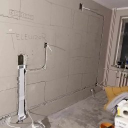 Coolwall Łukasz Rzepa - Ściana z płyt karton-gips z wyrysowanym miejscem na telewizor i poprowadzonymi kablami. Widoczne narzędzia i materiały budowlane. Etap prac wykończeniowych.