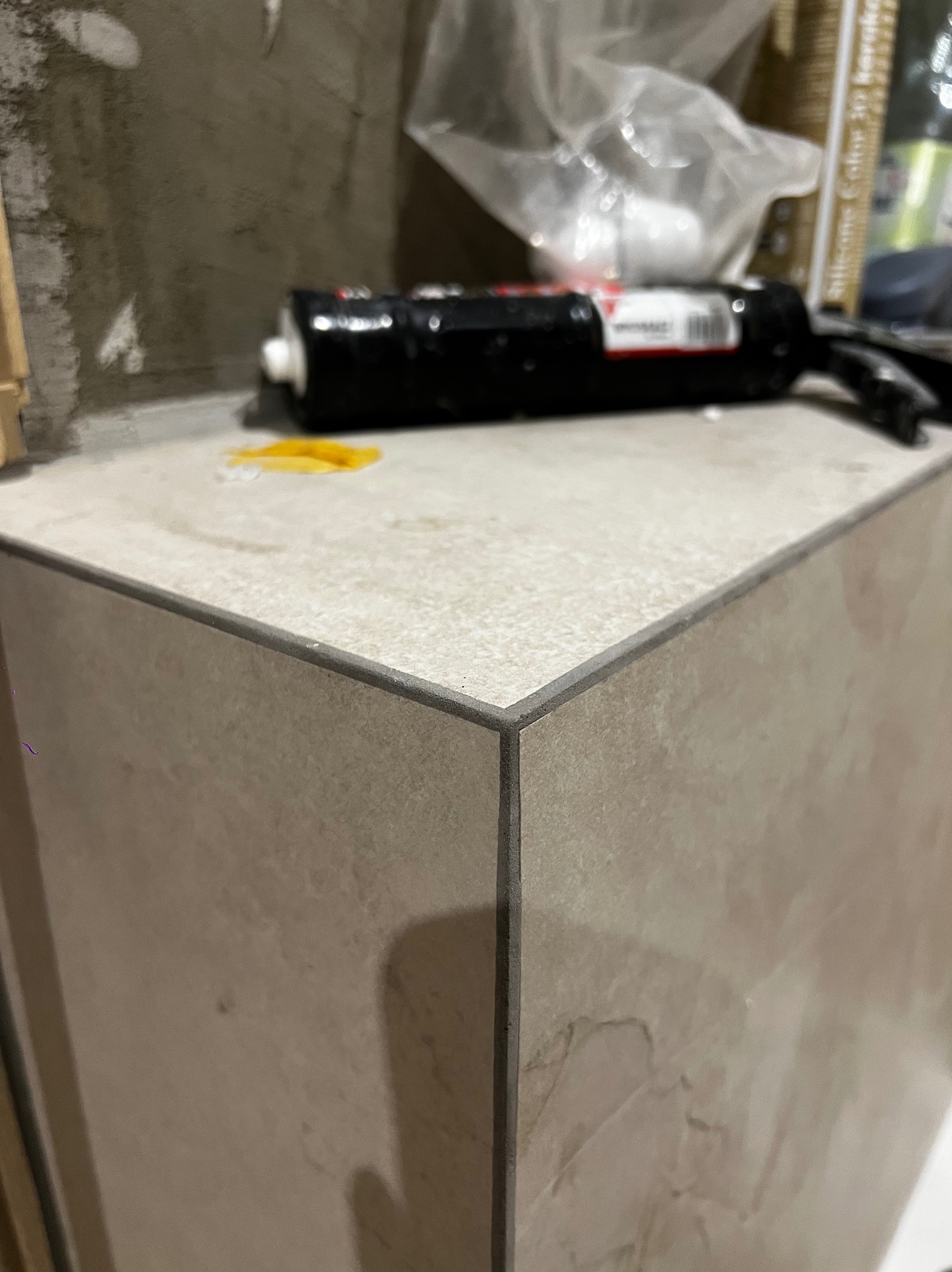 Wykończona obudowa z płytek ceramicznych, widoczny silikon i narzędzia. Detal narożnika z fugą. Prace glazurnicze w trakcie realizacji.