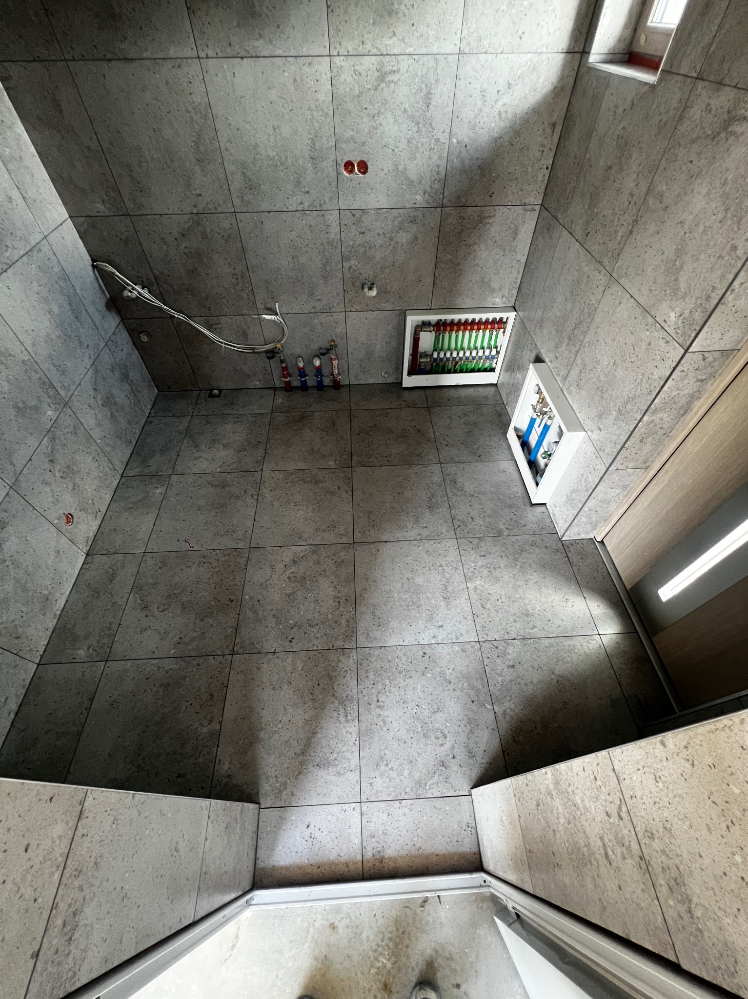 Wykończona łazienka z szarymi płytkami, widoczne instalacje wodne i elektryczne. Ujęcie z góry, podkreślające precyzję ułożenia płytek i estetykę wykończenia.