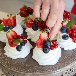 Cukiernia Koncepcyjna Julia Janczyk - Eleganckie mini bezy Pavlova z świeżymi owocami (truskawki, borówki, porzeczki) i miętą, układane na ozdobnej paterze przez kobiecą dłoń.