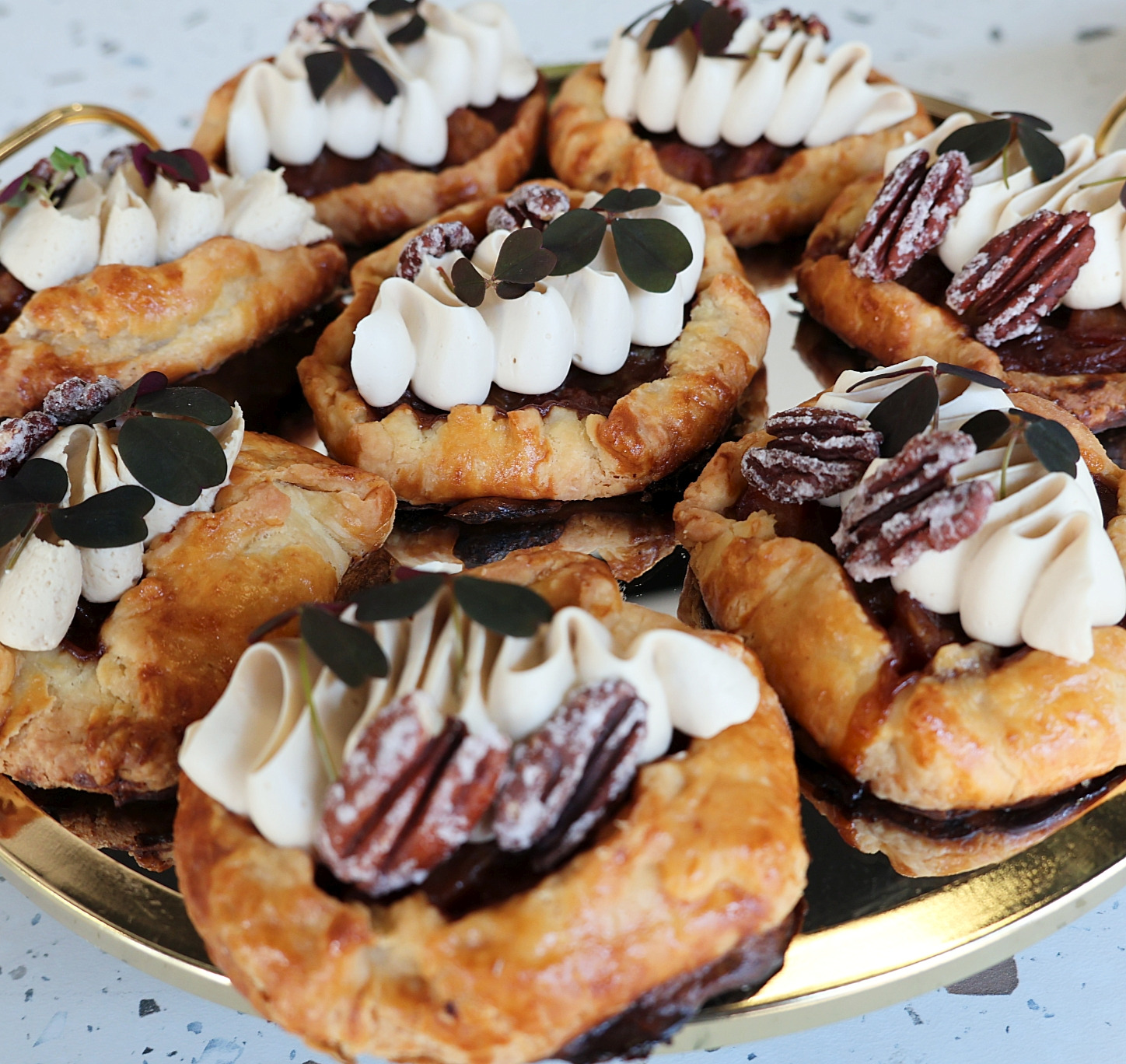 Apetyczne tartaletki na złotym talerzu: kruche ciasto, krem, orzechy pekan i listki. Idealne na deser lub słodki poczęstunek, z bliska.