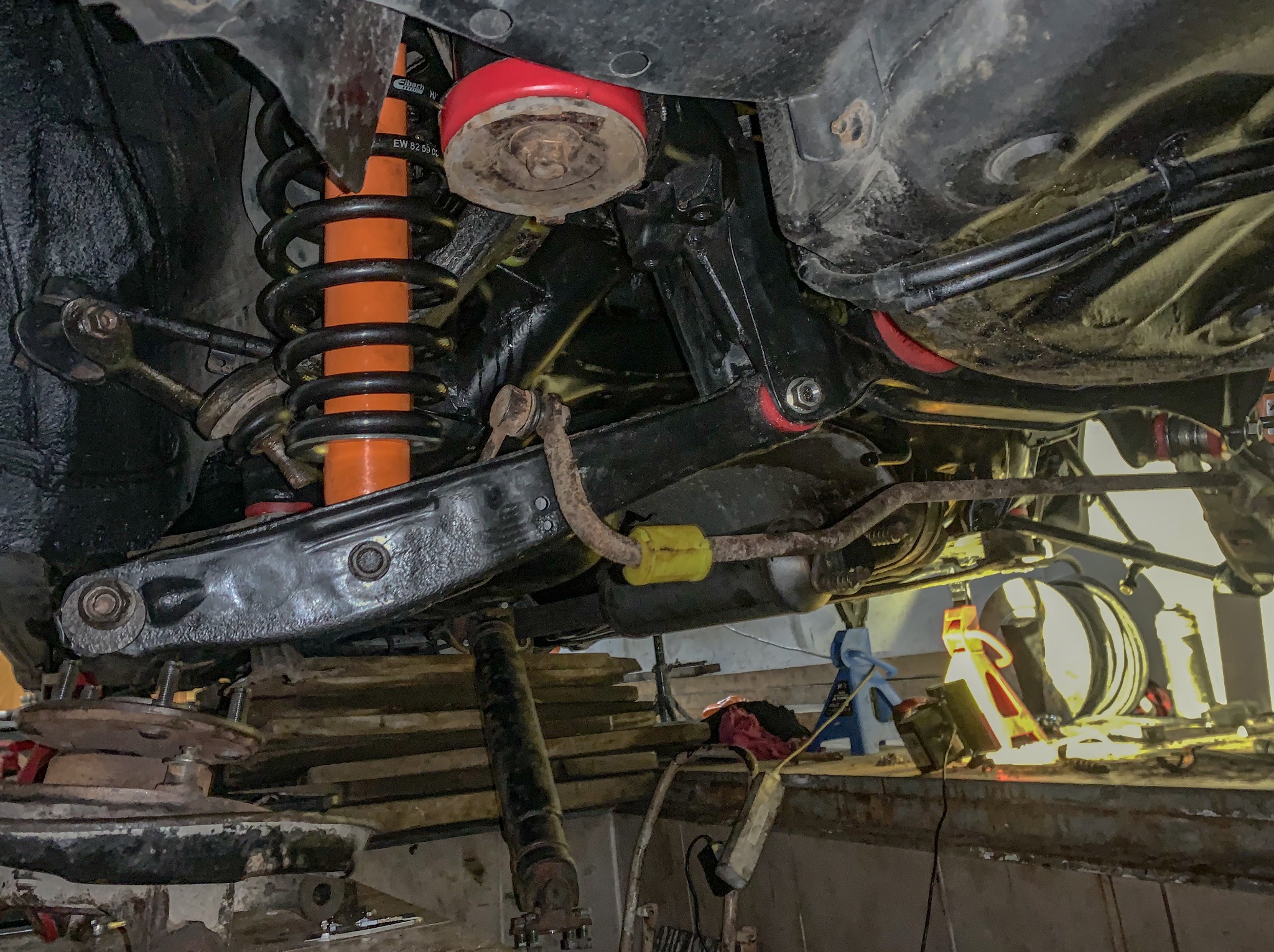 Zawieszenie samochodu Lexus IS200 po wymianie tulei na poliuretan, montażu sprężyn Eibach i amortyzatorów Koni. Widok od spodu, elementy zawieszenia w kolorze czarnym i pomarańczowym.