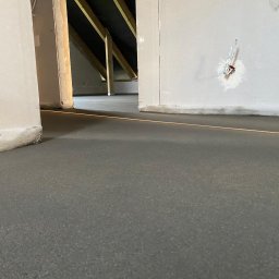 Mavo Invest Sp. z o.o. - Wylana, świeża posadzka jastrychowa w Będzinie, z widocznymi elementami konstrukcji dachu i ścian. Laserowy wskaźnik poziomu. Szary, gładki beton.