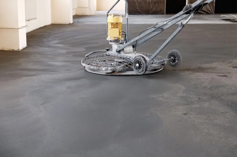 Szlifowanie posadzki jastrychowej za pomocą maszyny. Widoczne ślady po szlifowaniu i kolumny w tle. Jasne wnętrze.