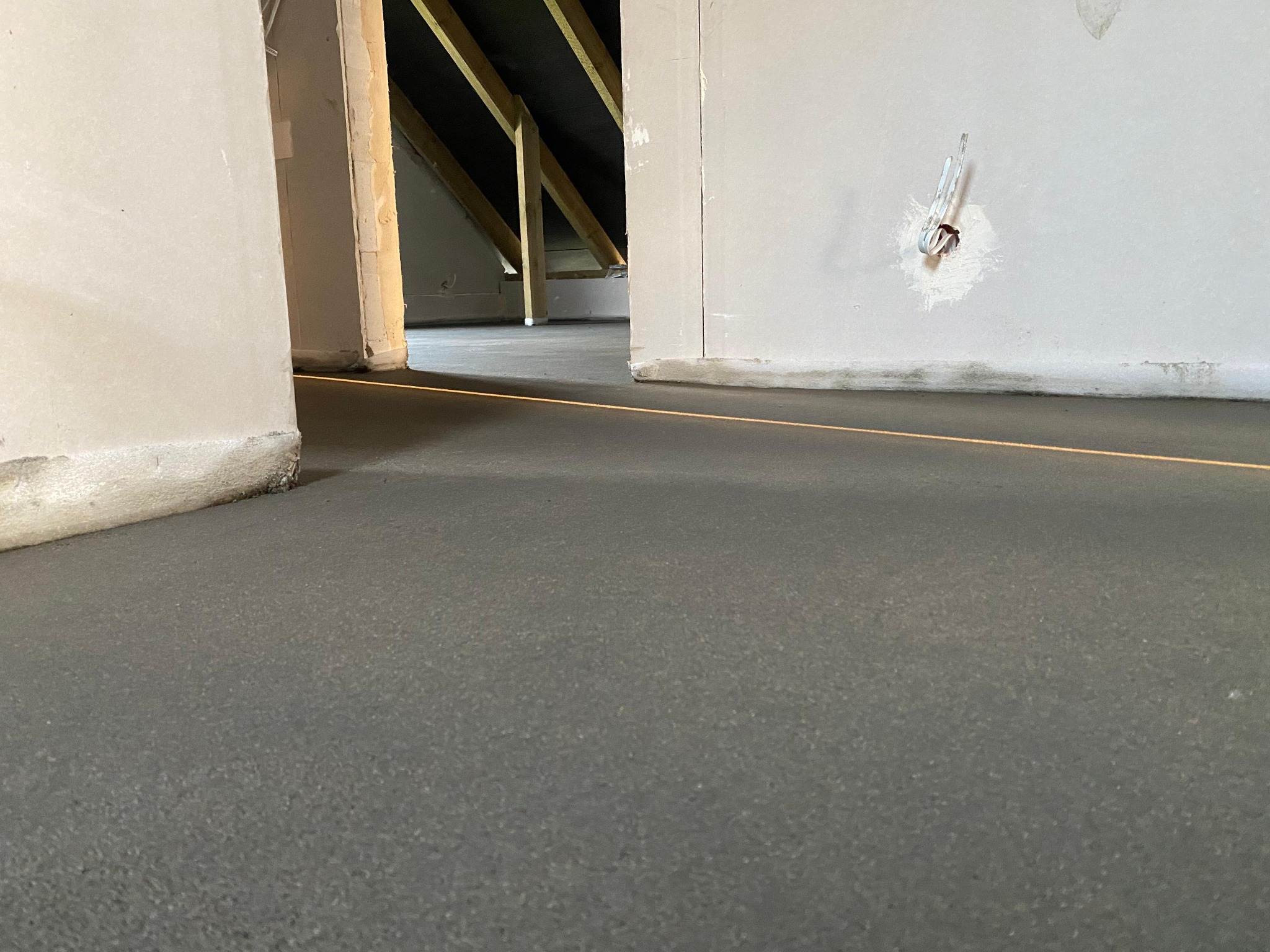 Wylana, świeża posadzka jastrychowa w Będzinie, z widocznymi elementami konstrukcji dachu i ścian. Laserowy wskaźnik poziomu. Szary, gładki beton.