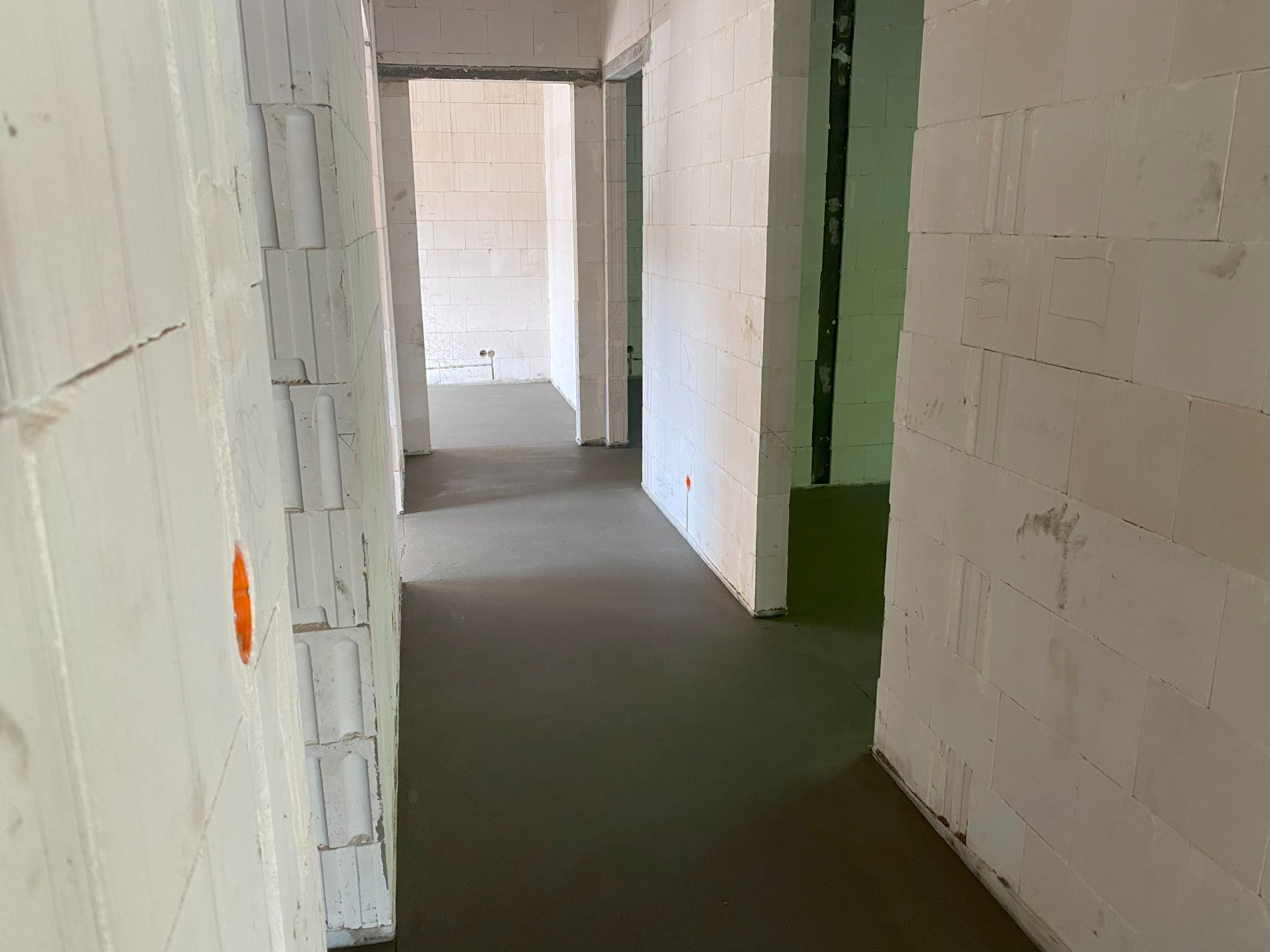 Świeżo wylana, gładka posadzka jastrychowa w surowym wnętrzu budynku z białymi ścianami z betonu komórkowego. Widoczne otwory instalacyjne.