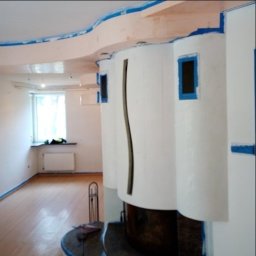 IURII PYNKO - Wnętrze pokoju w trakcie remontu: ściany i sufit zabezpieczone taśmą malarską, widoczny kominek z kolumnami, przygotowany do malowania lub gładzi.