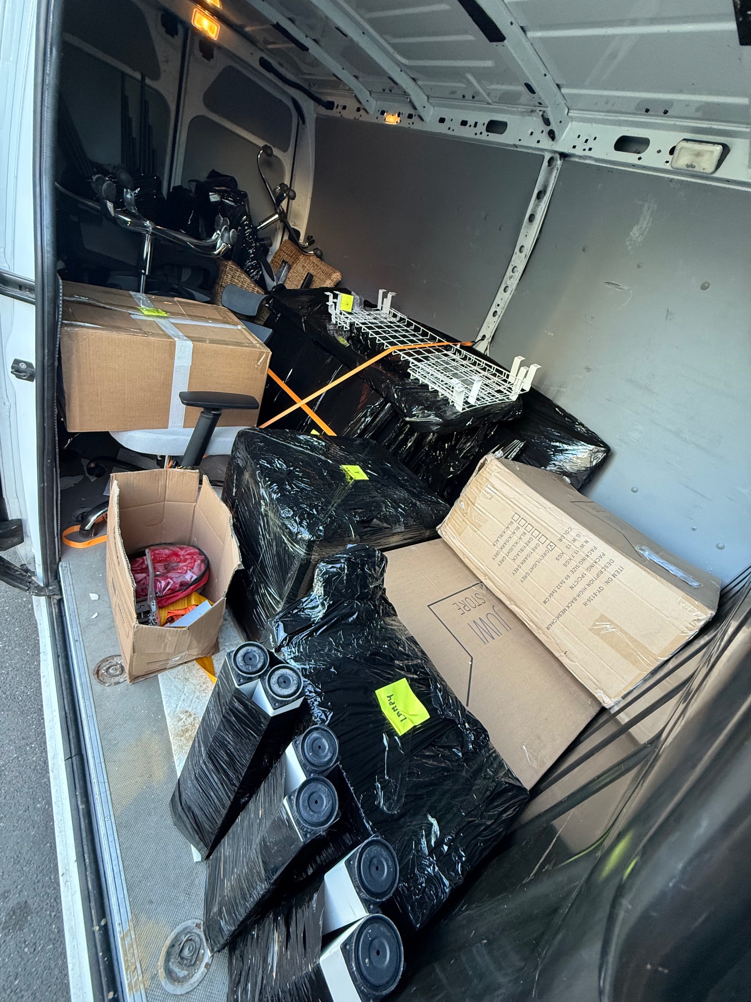 Wnętrze busa wypełnione kartonami, krzesłami biurowymi i zabezpieczonym sprzętem, gotowe do transportu. Widoczne detale pakowania i elementy wyposażenia.