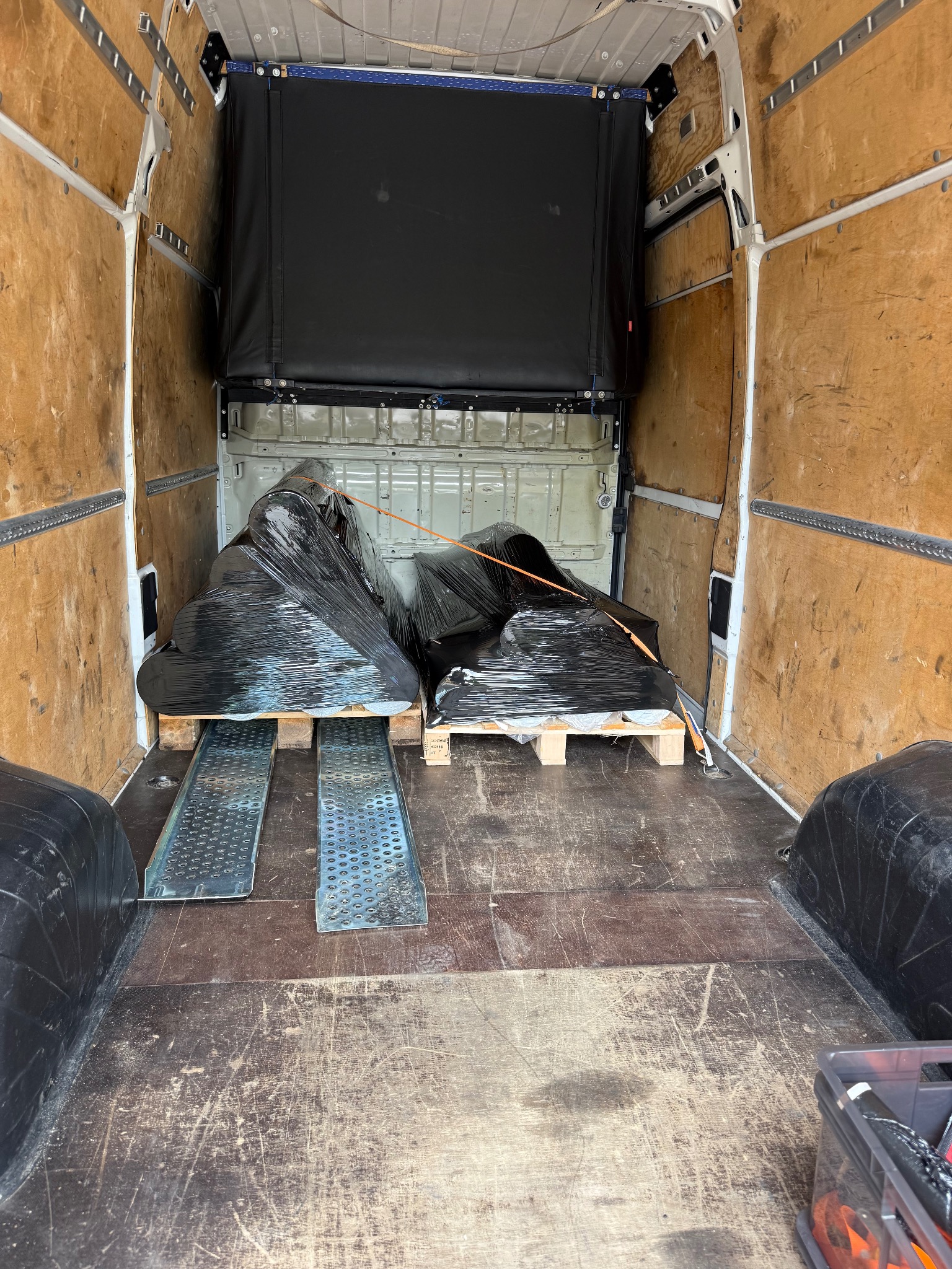 Wnętrze furgonetki z ładunkiem zabezpieczonym folią na paletach, gotowym do transportu. Widoczne najazdy i narzędzia w skrzynce.