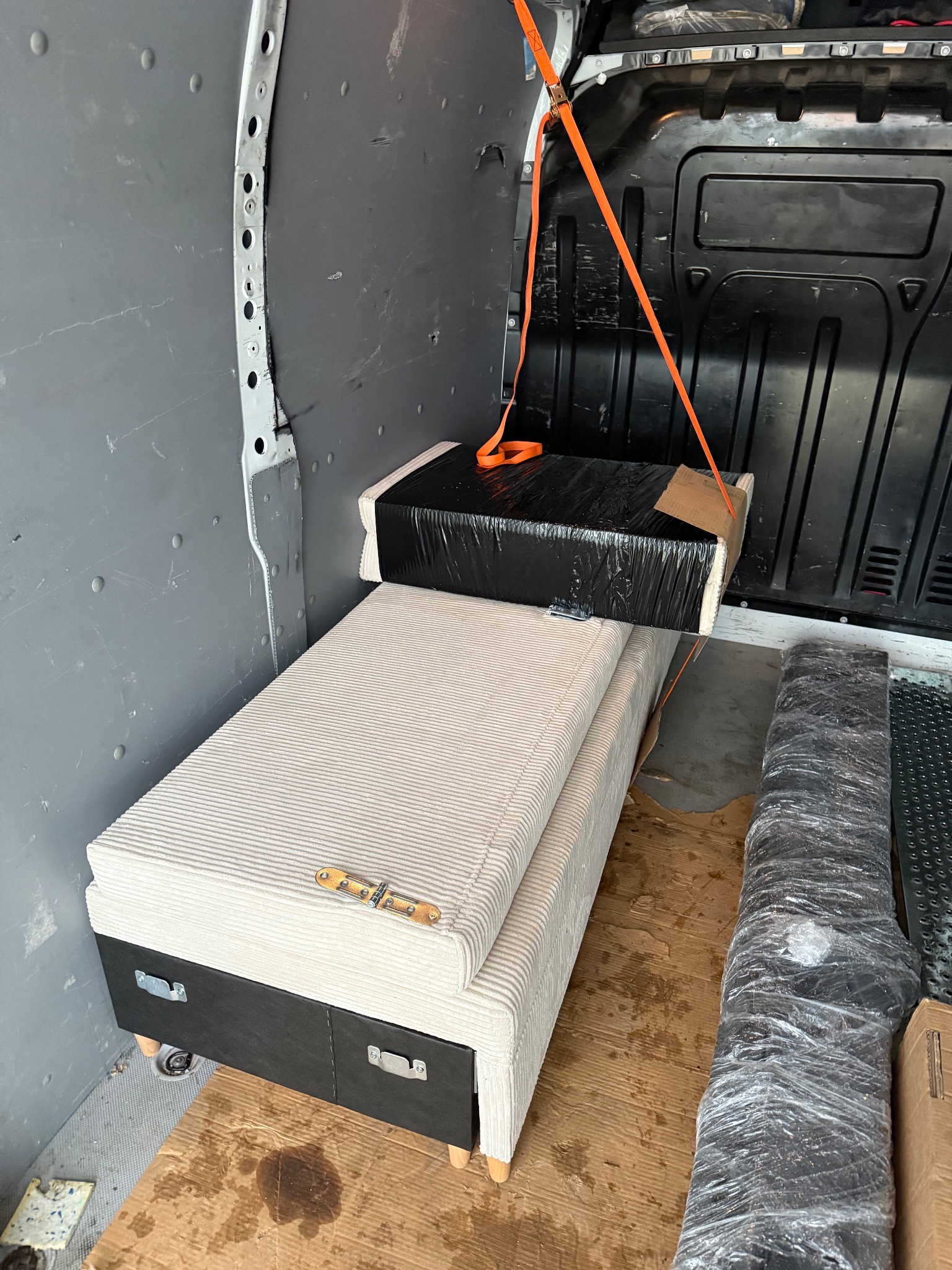 Meble zabezpieczone pasami wewnątrz paki busa podczas transportu. Widoczny tapicerowany tapczan z szufladami i folią owinięty element.