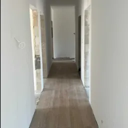 Wykończony korytarz z panelami podłogowymi imitującymi drewno i świeżo pomalowanymi na biało ścianami. Widoczne surowe ościeżnice drzwi.