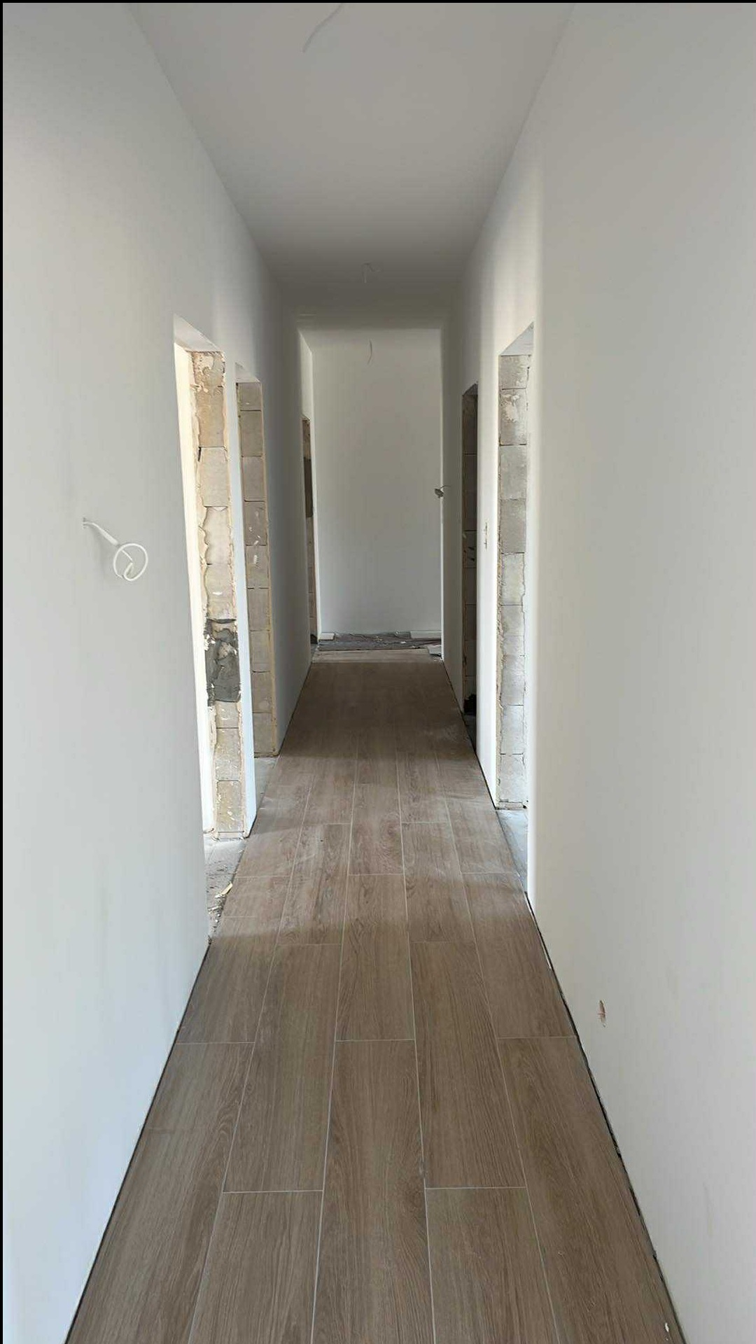 Wykończony korytarz z panelami podłogowymi imitującymi drewno i świeżo pomalowanymi na biało ścianami. Widoczne surowe ościeżnice drzwi.