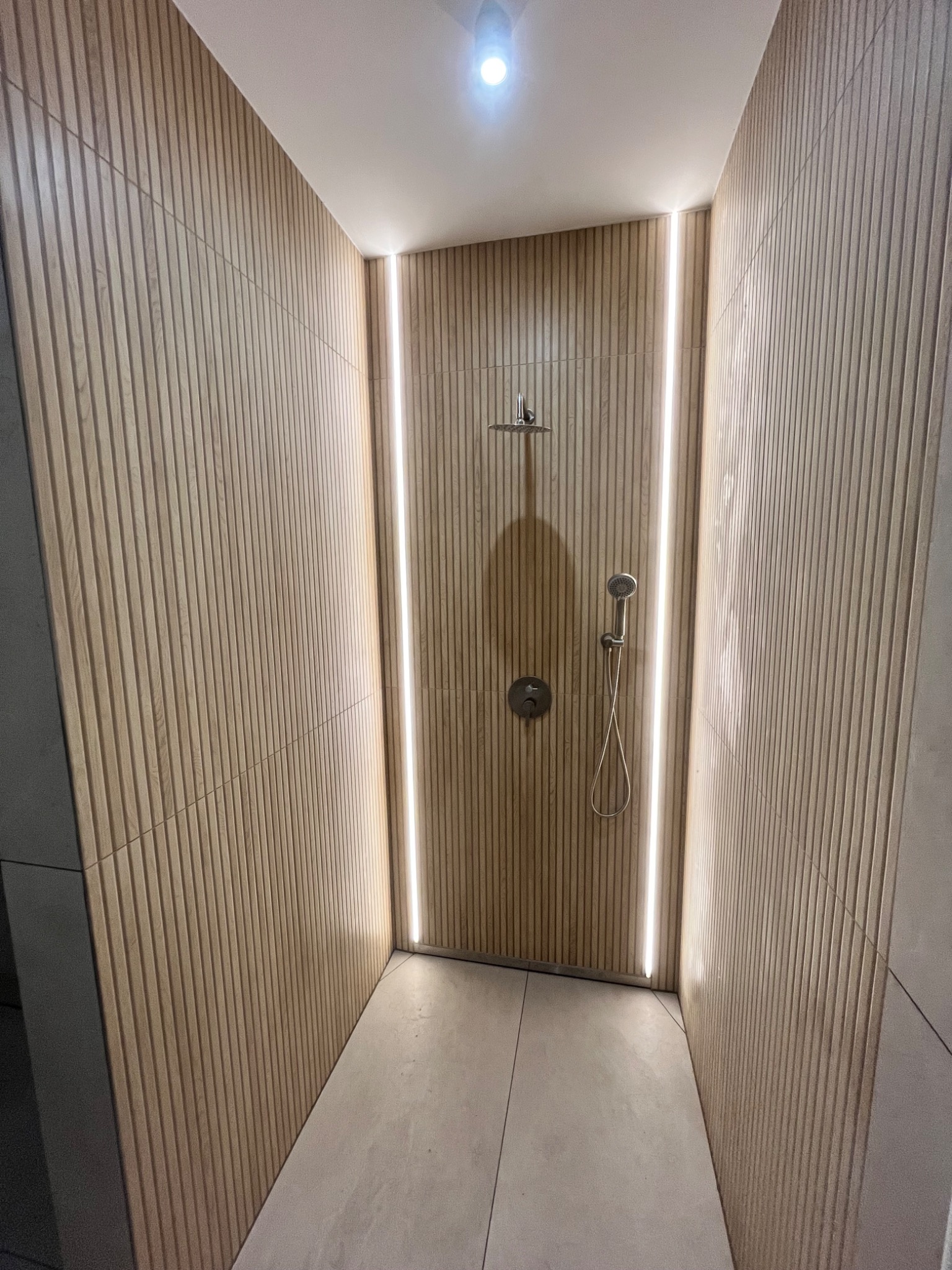 Kabina prysznicowa z panelami ściennymi w odcieniach drewna, podświetlona pionowymi pasami LED, z deszczownicą i słuchawką prysznicową.