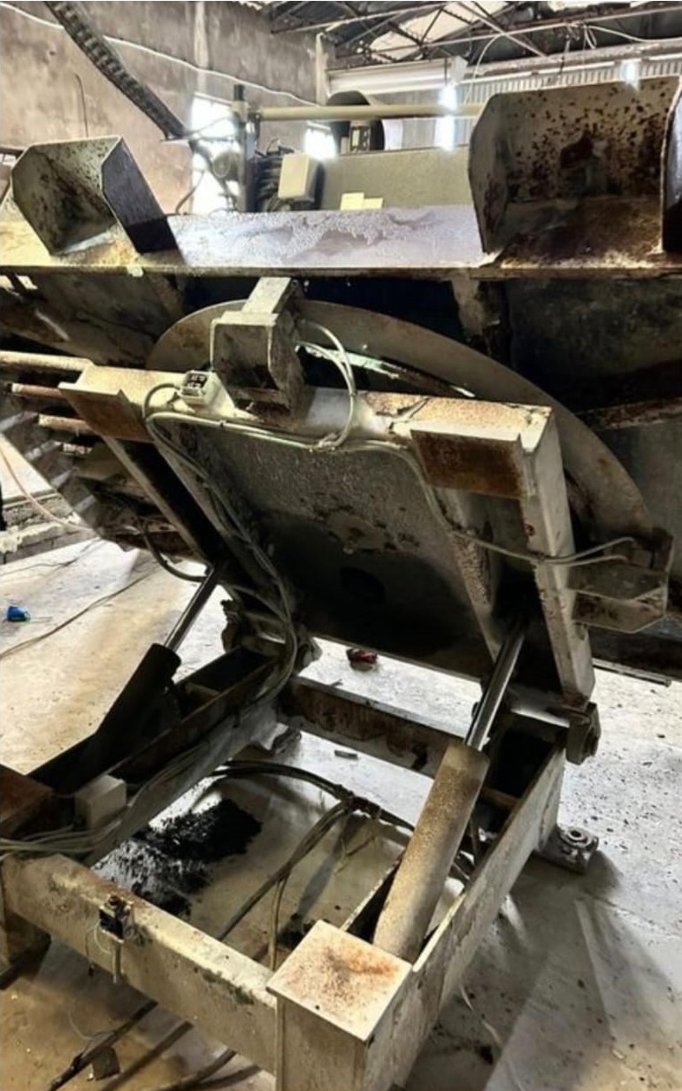 Metalowa maszyna przemysłowa z hydraulicznymi cylindrami, widoczne ślady korozji i zużycia, wnętrze hali produkcyjnej w tle.