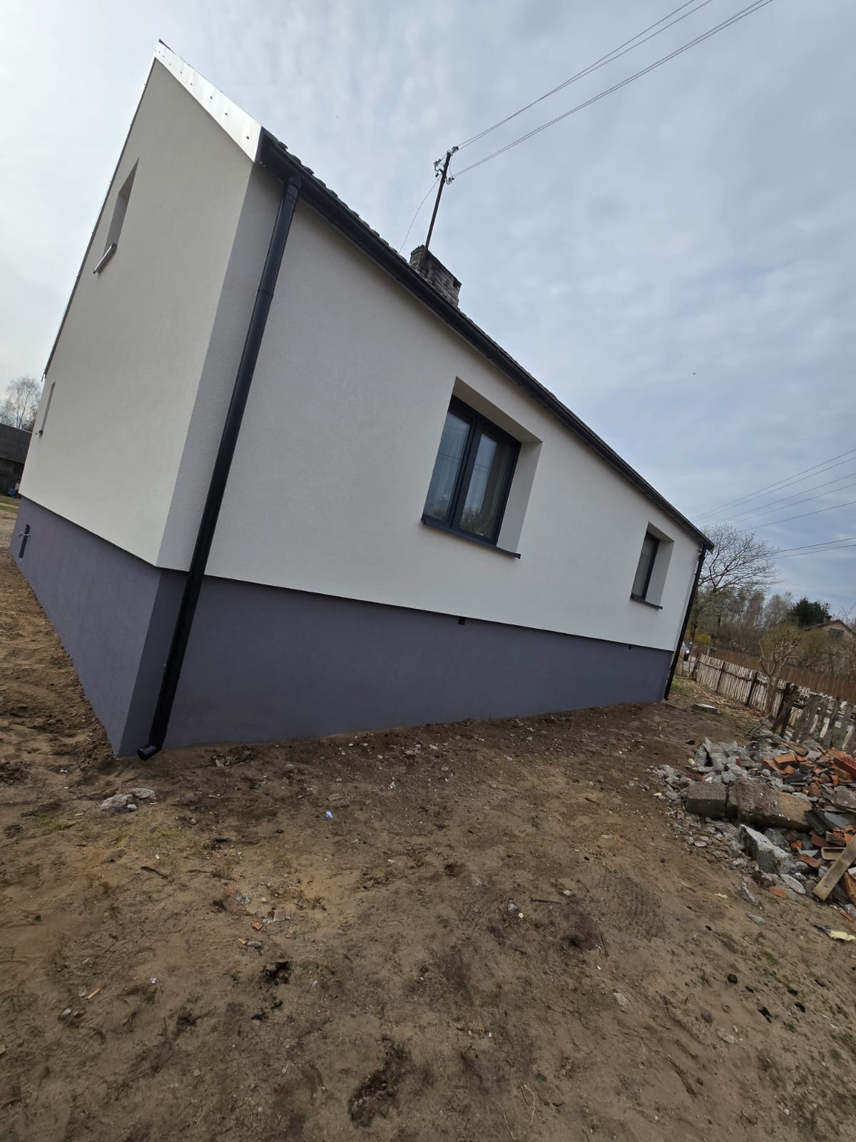 Dwukolorowa elewacja domu jednorodzinnego po renowacji, z widocznymi czarnymi oknami i rynnami. Ujęcie z dołu podkreśla świeżość i nowoczesny wygląd budynku.