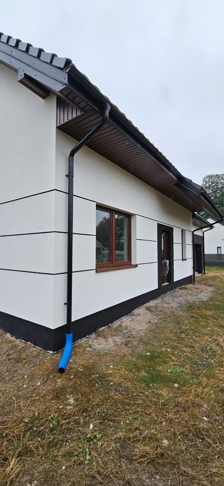 Elewacja domu jednorodzinnego z białymi ścianami i czarnymi akcentami, widok z boku, rynna z niebieskim zakończeniem. Nowoczesny styl.