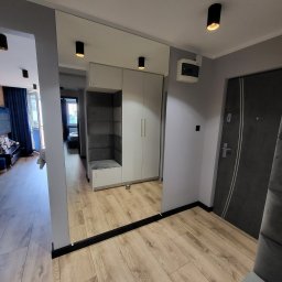 EAST-WOOD Patryk Goławski - Duże lustro w przedpokoju z wbudowaną szafą i siedziskiem, czarne listwy przypodłogowe, panele podłogowe imitujące drewno, oświetlenie punktowe.