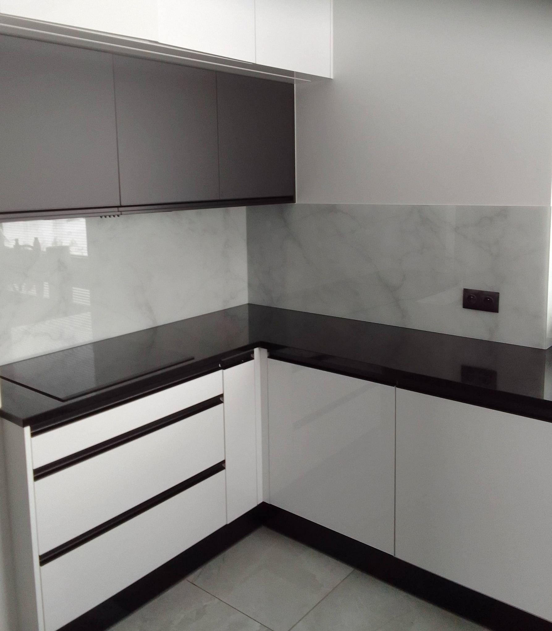 Kuchenna zabudowa: białe szafki z czarnymi akcentami, czarny blat i marmurowe panele szklane na ścianie. Nowoczesny design, minimalistyczny styl.