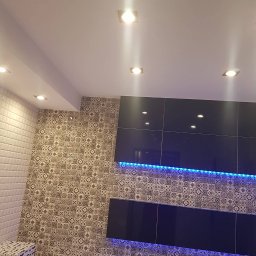 Ernest - Wykończona ściana z mozaiką i czarnymi szafkami podświetlonymi niebieskim LED, oświetlenie sufitowe punktowe, białe płytki na ścianie, dekoracyjny kosz.