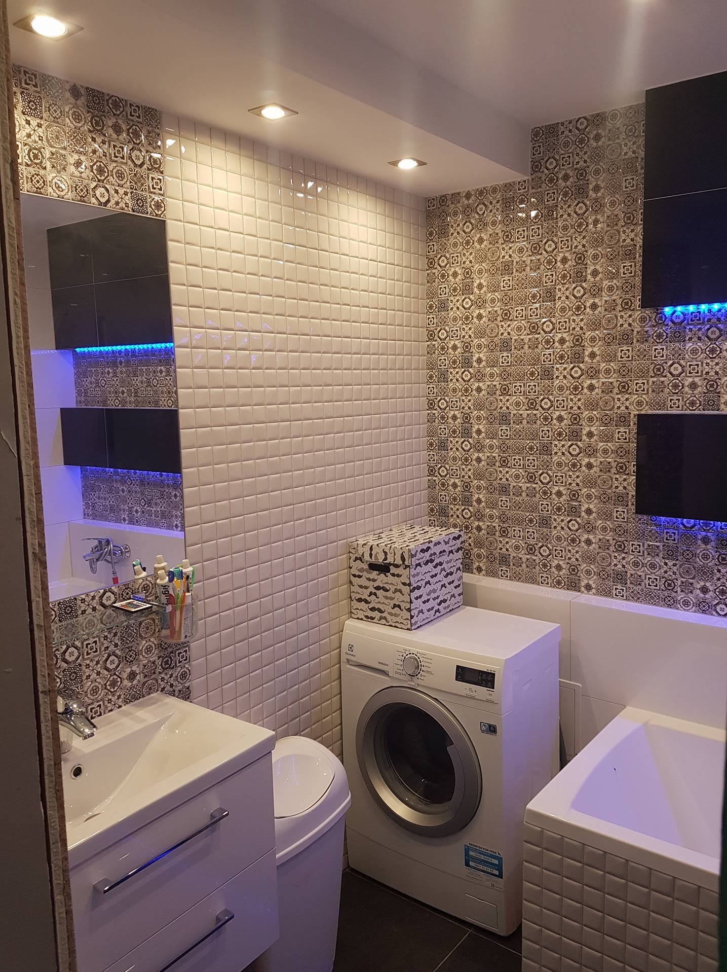 Wnętrze łazienki po remoncie: białe płytki na ścianach, wzorzysta mozaika, umywalka z szafką, pralka i wanna. Całość oświetlona punktowymi lampami sufitowymi.
