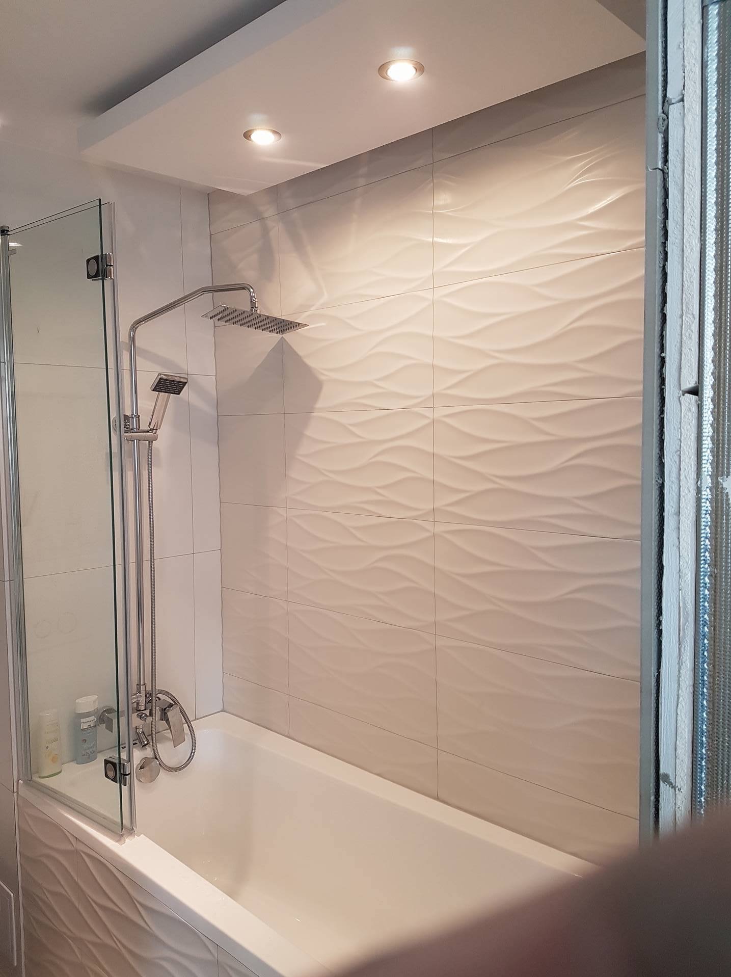 Nowoczesna łazienka z wanną, szklanym parawanem i deszczownicą. Płytki o falującej strukturze na ścianie. Oświetlenie punktowe sufitowe.