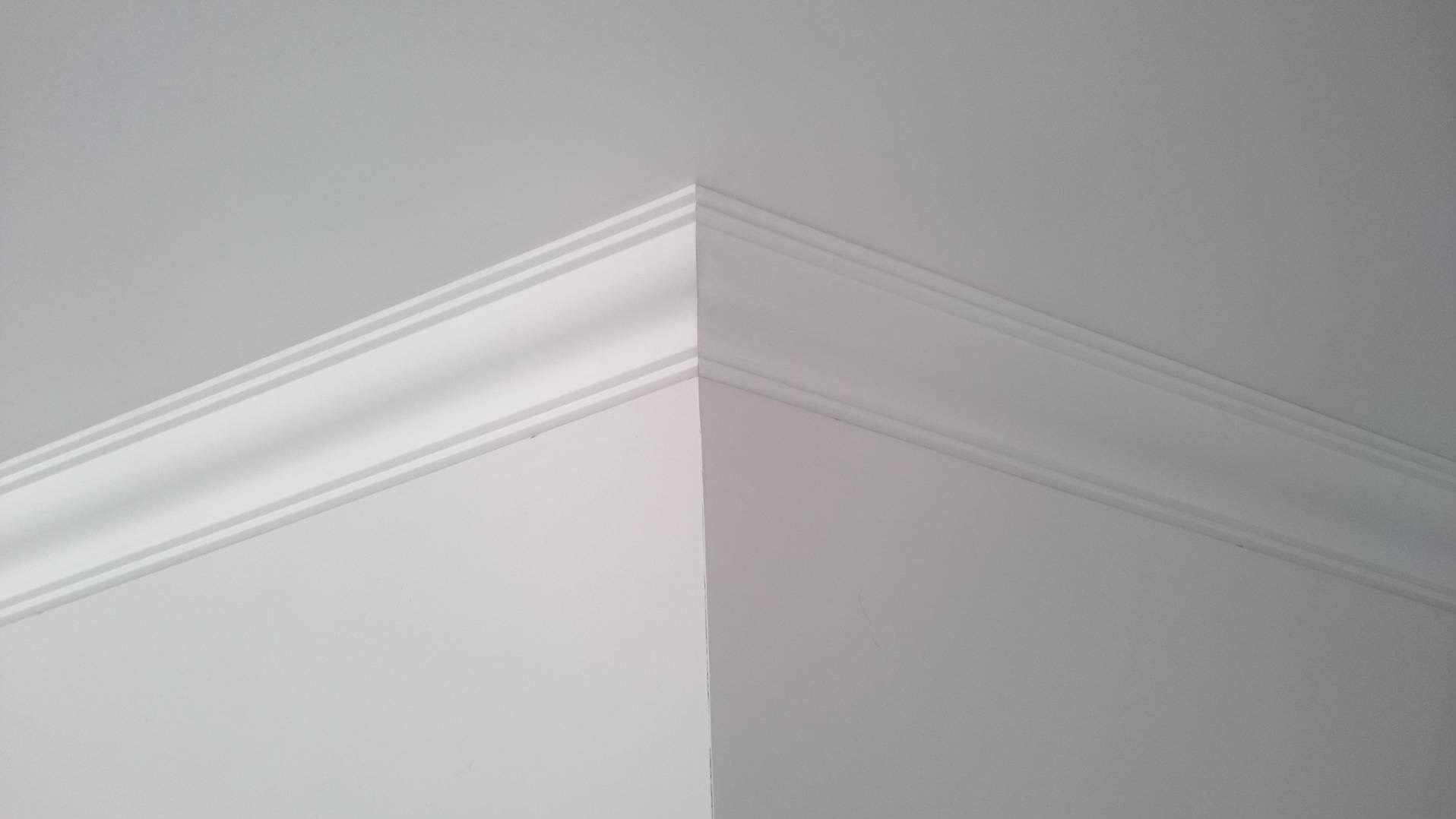 Detal wykończenia wnętrza: biała listwa dekoracyjna na styku ściany i sufitu, precyzyjnie zamontowana w rogu pomieszczenia.