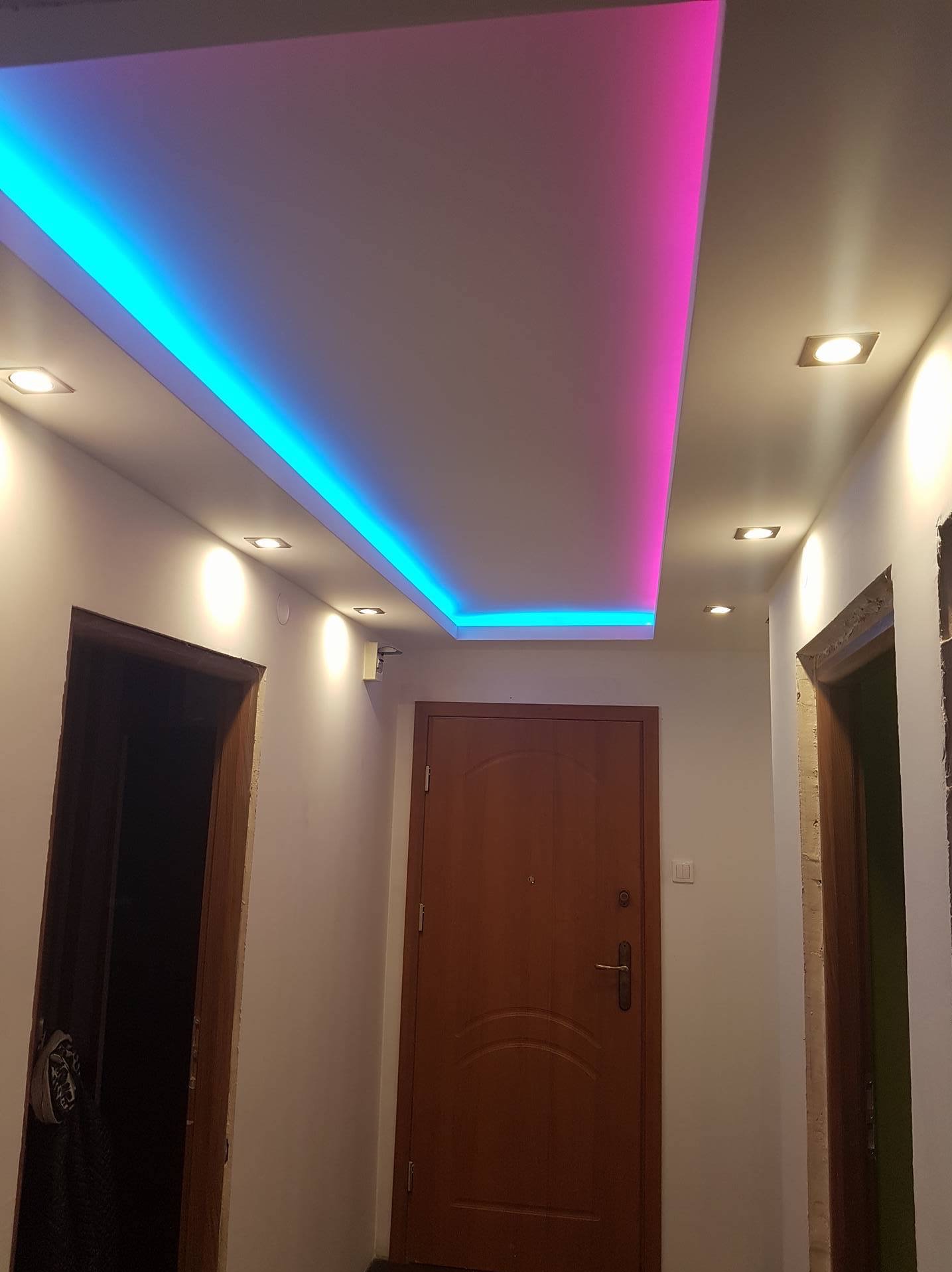 Podwieszany sufit z oświetleniem LED w kolorach niebieskim i różowym w przedpokoju, widoczne drzwi wejściowe i ościeżnice.