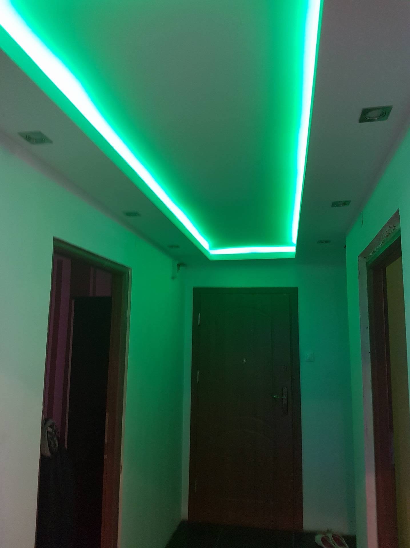 Korytarz z podwieszonym sufitem i oświetleniem LED w kolorze zielonym. Widoczne drzwi wejściowe i ościeżnice drzwi wewnętrznych. Świecąca listwa LED.