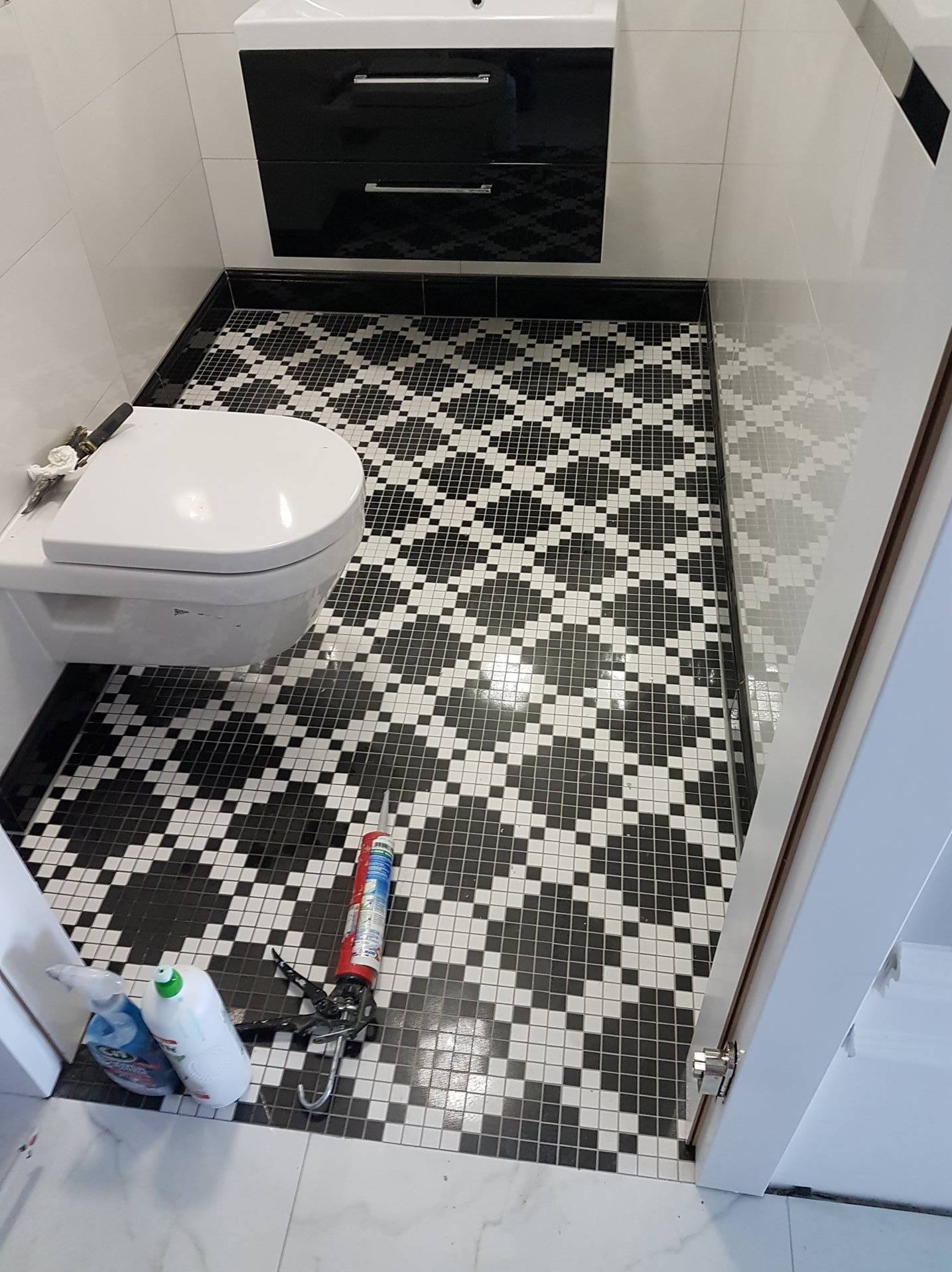 Łazienka po remoncie: czarno-biała mozaika na podłodze, wisząca toaleta i szafka z umywalką. Widoczne narzędzia glazurnicze.