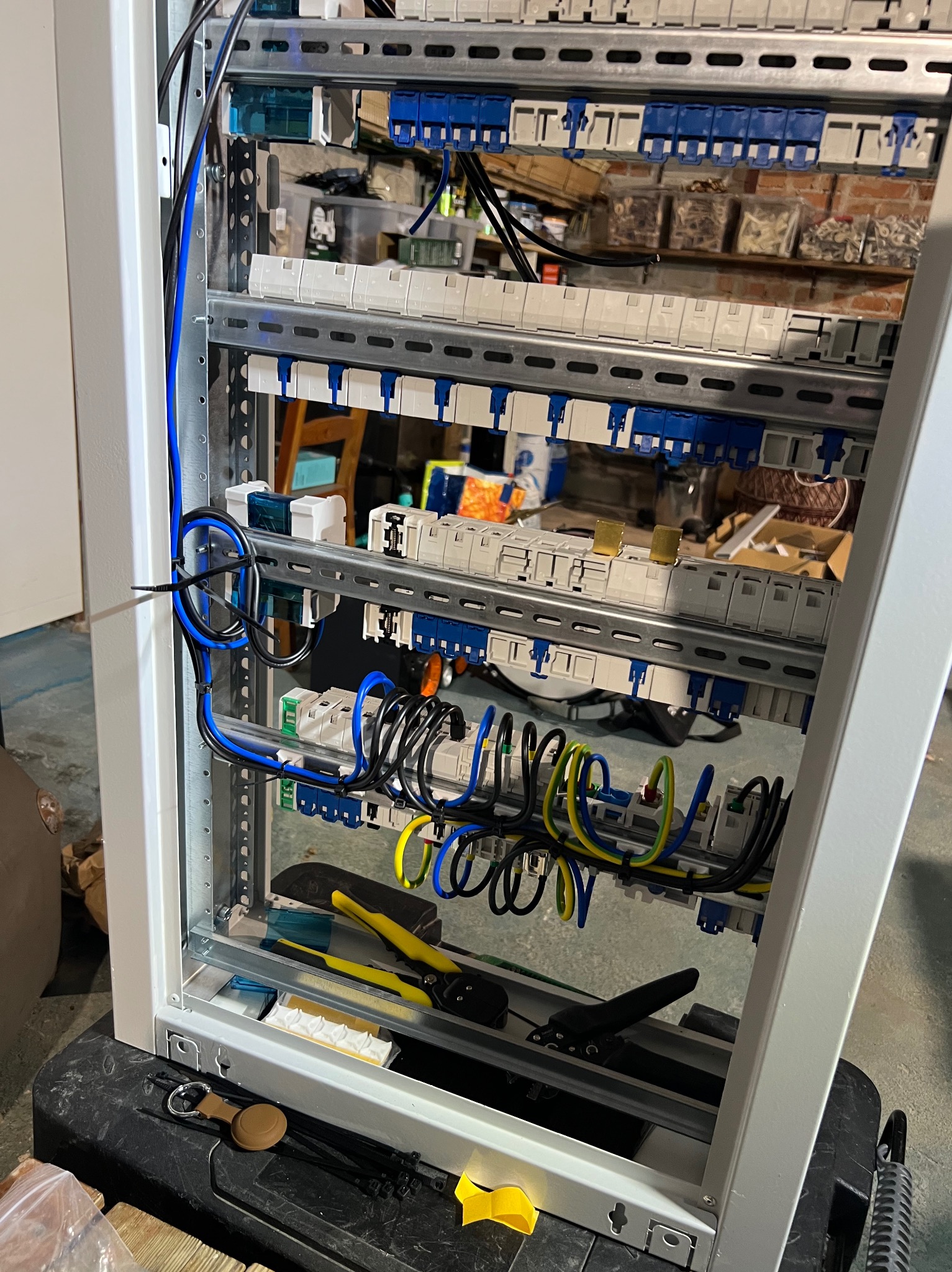 Rozdzielnica elektryczna w trakcie montażu: widoczne kable, bezpieczniki, listwy DIN i narzędzia. Przewody ułożone w pętle, częściowo zamocowane.