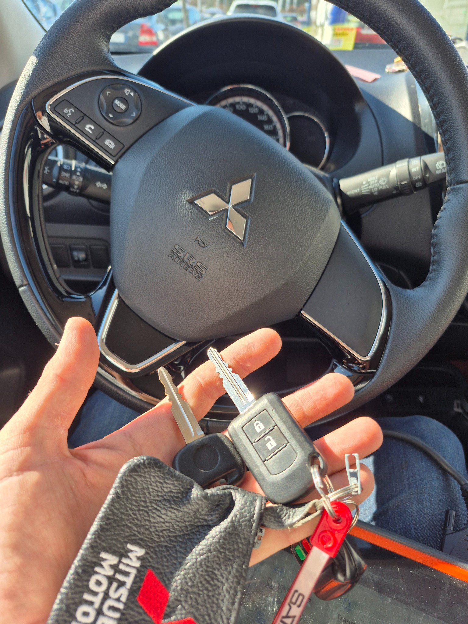 Kluczyki samochodowe Mitsubishi trzymane w dłoni na tle kierownicy, potencjalnie dorabianie kluczy lub awaryjne otwieranie auta.