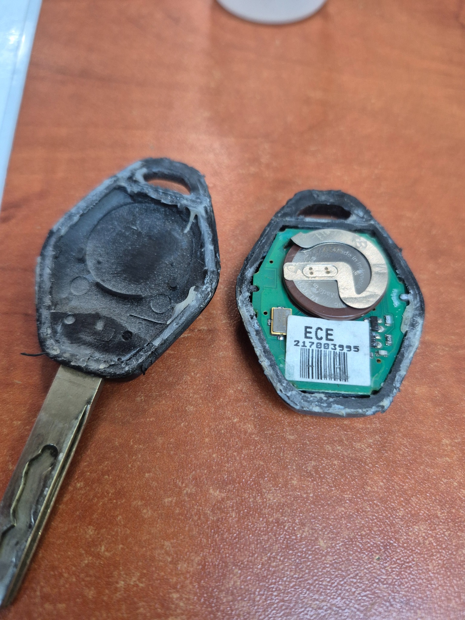 Otwarty kluczyk samochodowy z widoczną elektroniką i baterią, obok obudowa. Klucz po naprawie lub w trakcie wymiany obudowy.