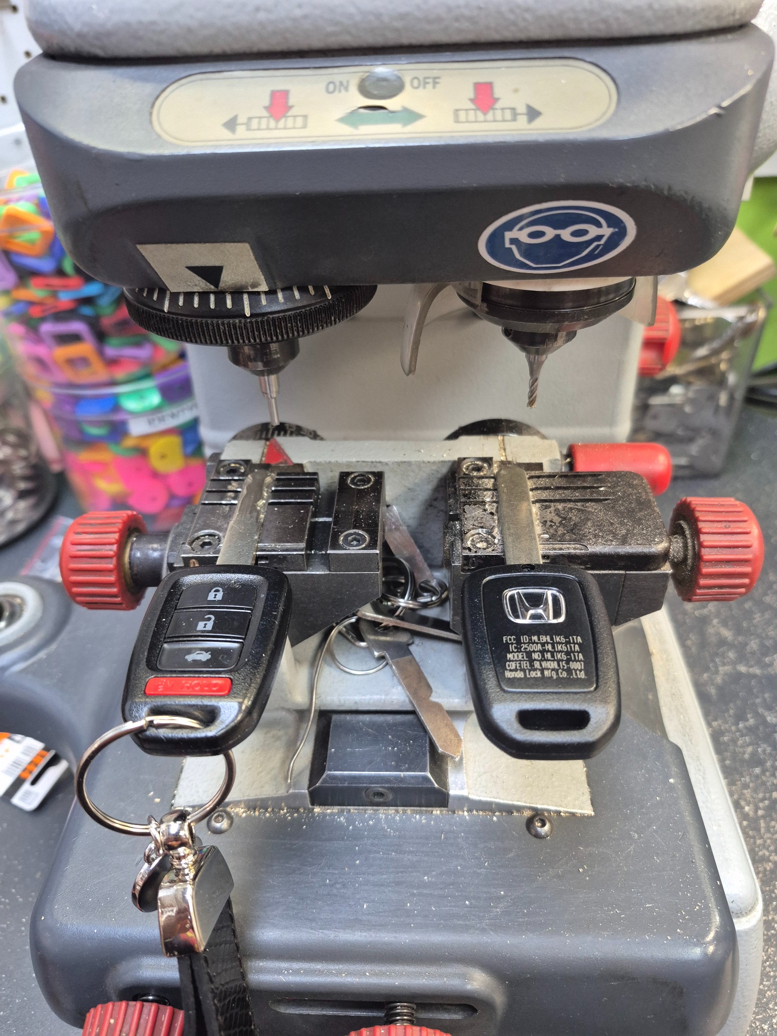 Kopiowanie kluczyka samochodowego Honda na maszynie. Dwa kluczyki umieszczone w uchwytach, wiertła gotowe do pracy. Kluczyk z pilotem, zbliżenie na proces dorabiania.