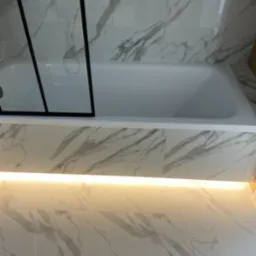 Biała wanna z czarną szybą kabiny, marmurowe płytki na ścianach i podłodze, podświetlenie LED pod wanną. Minimalistyczny design łazienki.