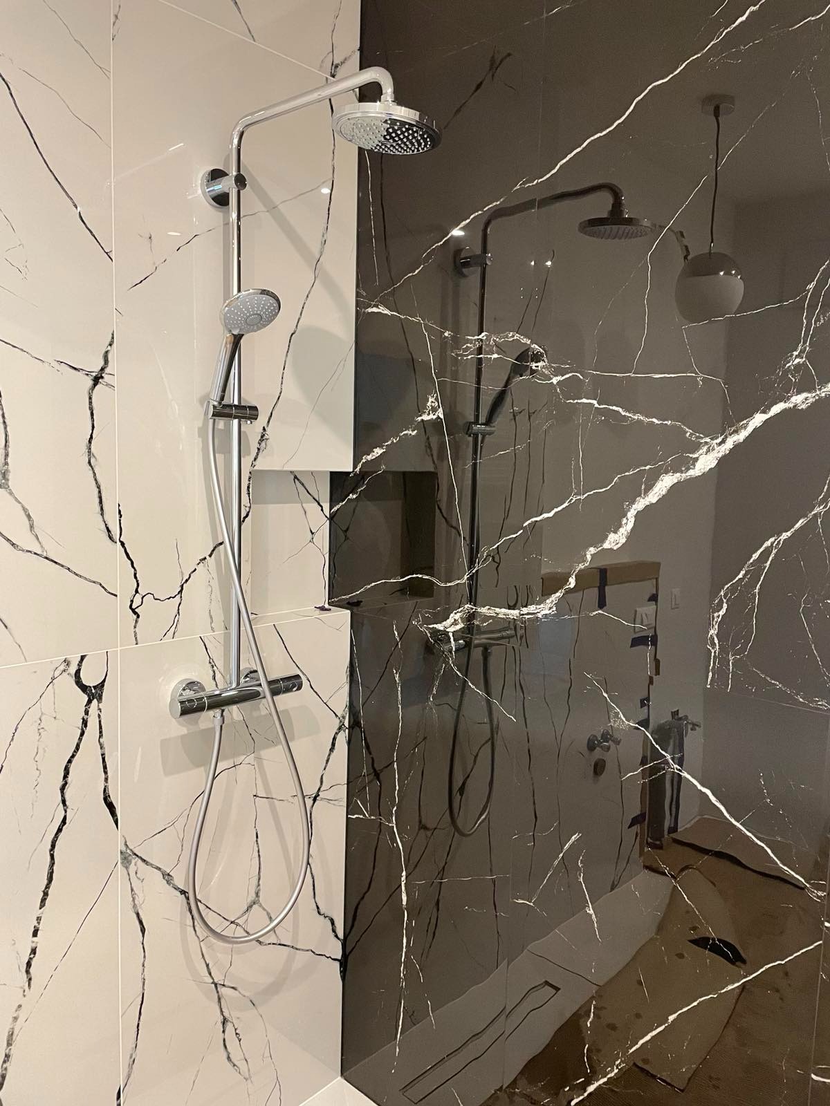 Nowoczesna kabina prysznicowa z chromowaną armaturą i płytkami imitującymi marmur w odcieniach bieli i antracytu, eleganckie wykończenie łazienki.