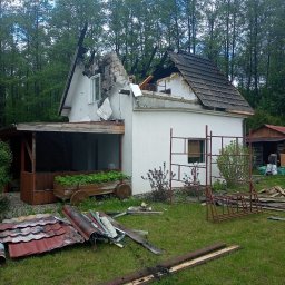 Usługi Ciesielsko- Dekarskie - Sebastian Augustynowicz - Uszkodzony dach i ściana domu po pożarze, widoczne rusztowania i pozostałości po remoncie na trawniku. Częściowo zniszczona konstrukcja dachu i elewacja.