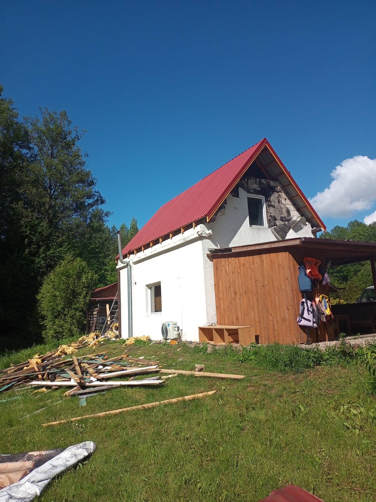 Czerwony dach na białym domu w Lidzbarku Warmińskim, częściowo zdemontowany, z widocznymi elementami konstrukcyjnymi i stertą odpadów budowlanych na trawniku.