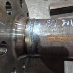 Welding and Metalworks Sebastian Piekarczyk - Spoina obwodowa rury ze stalowym kołnierzem, widoczne ślady spawania TIG i białe napisy na rurze, szlifowana powierzchnia kołnierza
