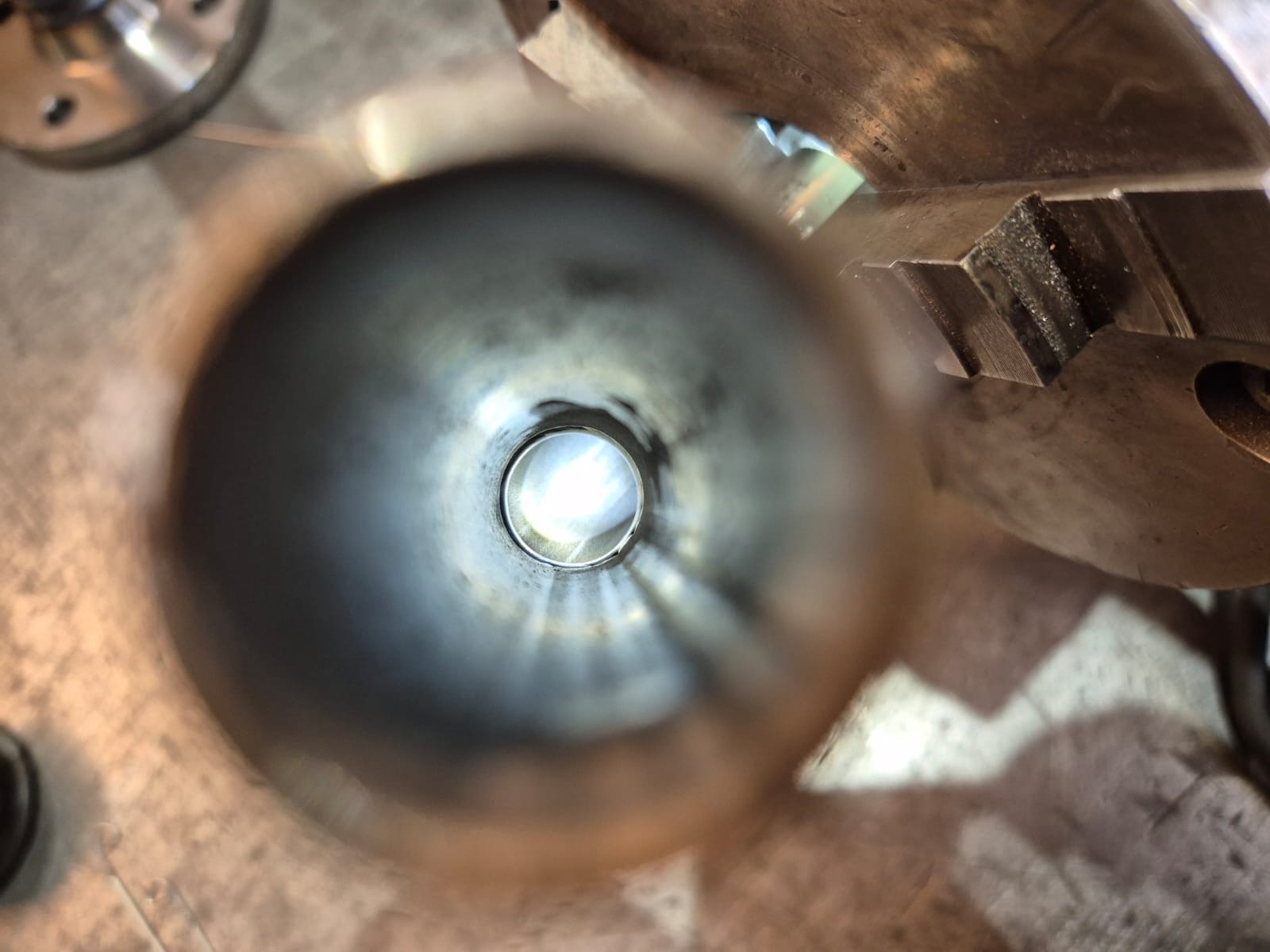 Wnętrze metalowej rury, widok z perspektywy, z fragmentami narzędzi obróbczych w tle. Widoczny proces wykańczania, szlifowania lub czyszczenia wnętrza rury.