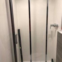 Dmytrów Andrzej - Kabina prysznicowa z chromowanymi profilami i poziomica wewnątrz, białe płytki na ścianach, bateria umywalkowa. Widok na wnętrze kabiny.