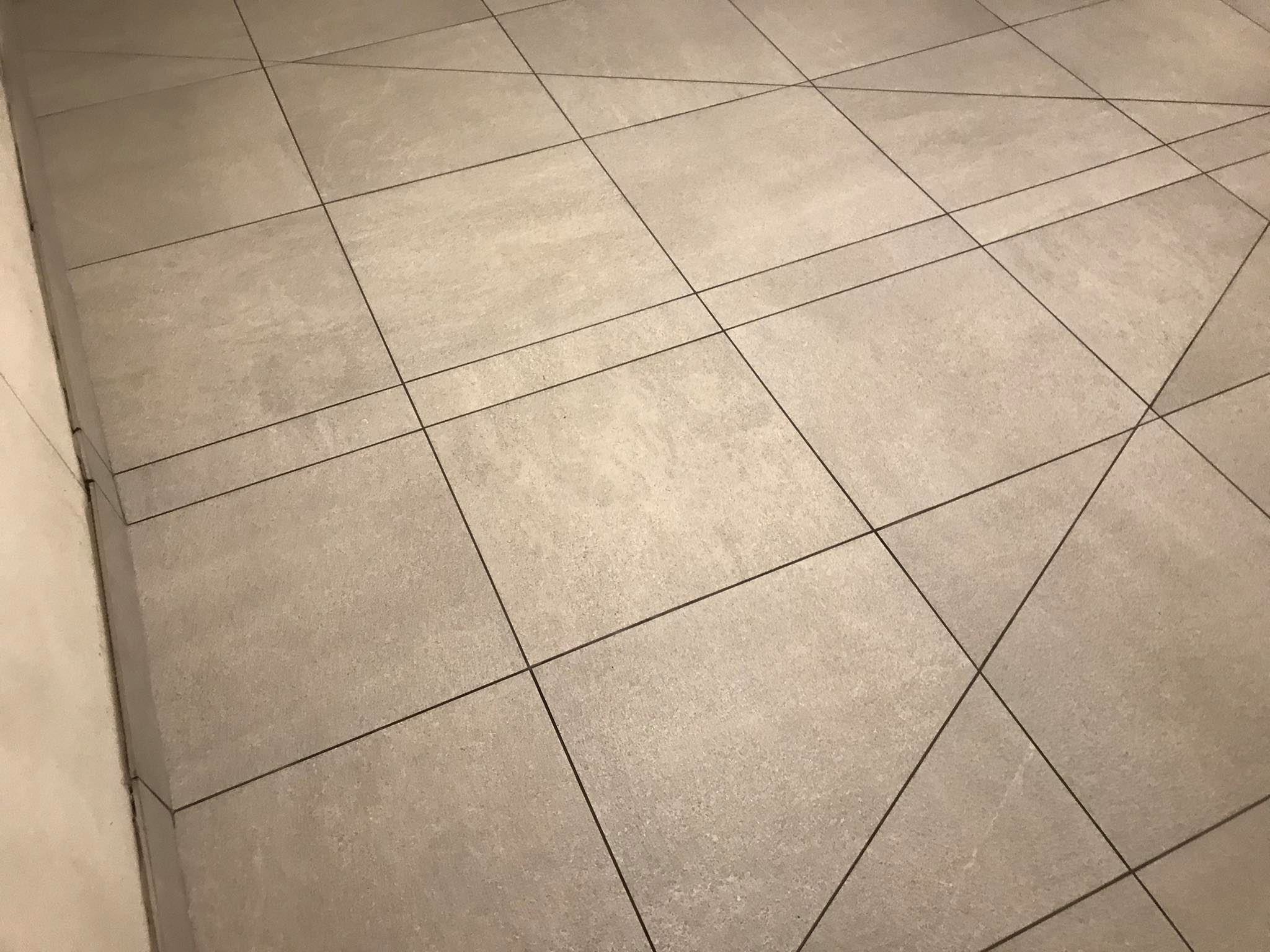 Jasnoszare, kwadratowe płytki podłogowe ułożone z ciemnoszarą fugą, widoczne z bliska pod kątem. Minimalistyczny wzór i faktura płytek.