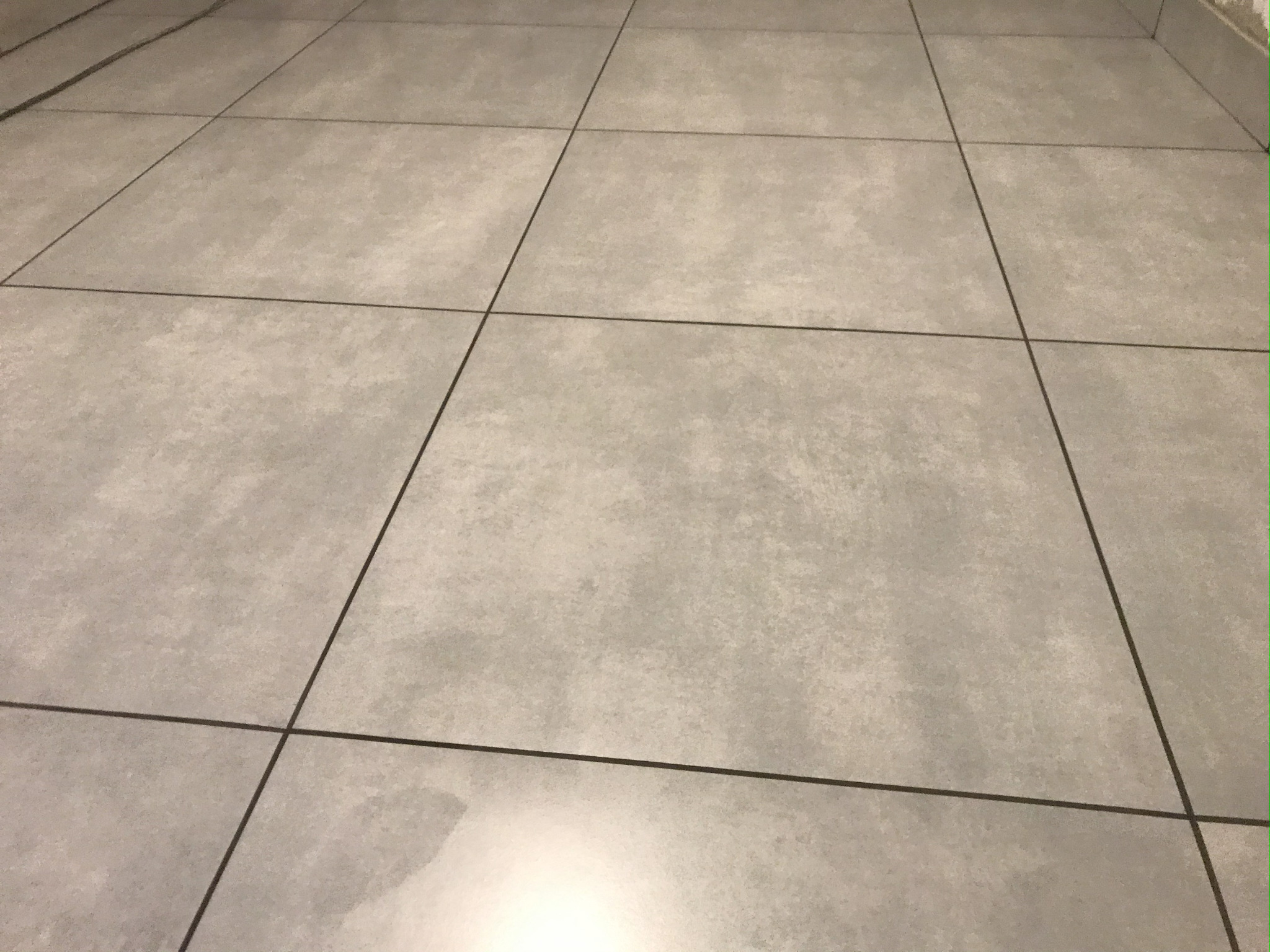 Jasnoszare płytki podłogowe z ciemnymi fugami ułożone w regularny wzór, widok z góry. Minimalistyczny design, gładka powierzchnia, odbicie światła.