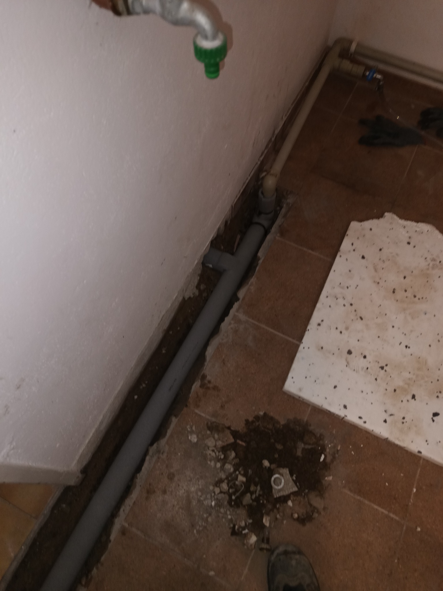 Szare rury CO w bruździe w podłodze, etap wymiany instalacji w starym budownictwie w Poznaniu. Widoczny kran i płytki podłogowe.