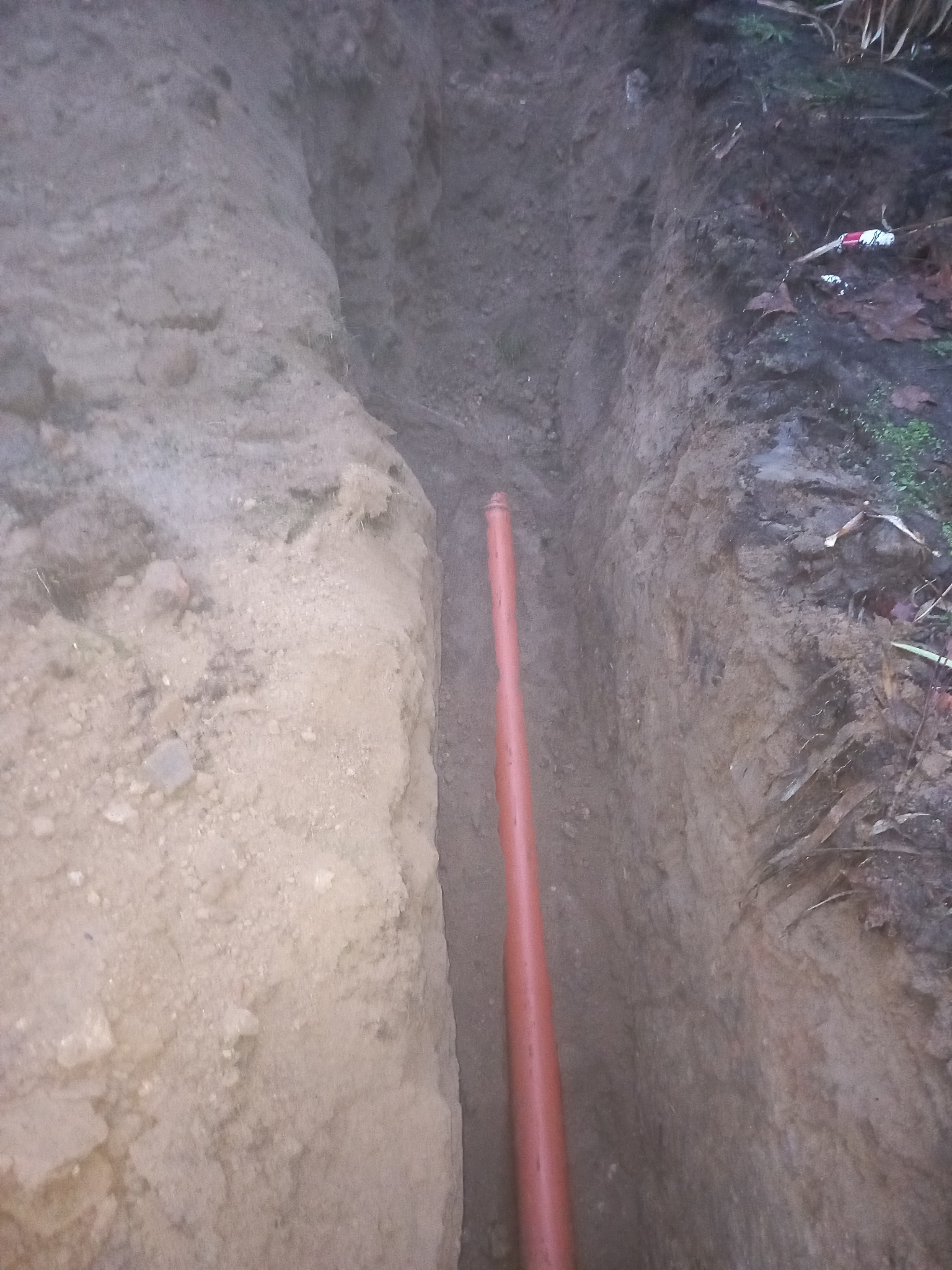 Wkopana w ziemię rura z tworzywa sztucznego w wykopie, prawdopodobnie część instalacji wodno-kanalizacyjnej lub grzewczej, widok z góry na wykop.