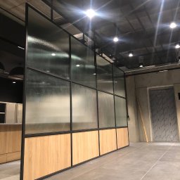 ARTmeble - Nowoczesna ścianka działowa z matowego szkła i drewnianych paneli, czarne ramy, surowy industrialny design, widok z perspektywy podłogi.
