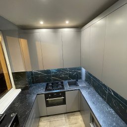 ARTmeble - Nowoczesna kuchnia w szarościach z czarnym blatem i backsplashiem imitującym marmur. Ujęcie z góry podkreśla układ zabudowy i oświetlenie punktowe.